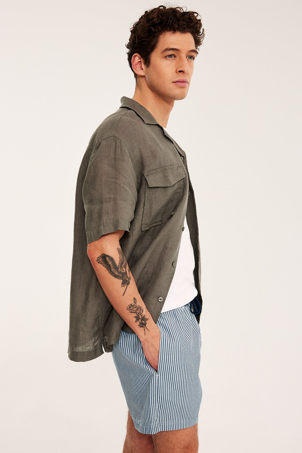 Sivukuva: mies yllään raidalliset tummansiniset seersucker-uimashortsit, valkoinen t-paita ja avoin tummanvihreä paita.