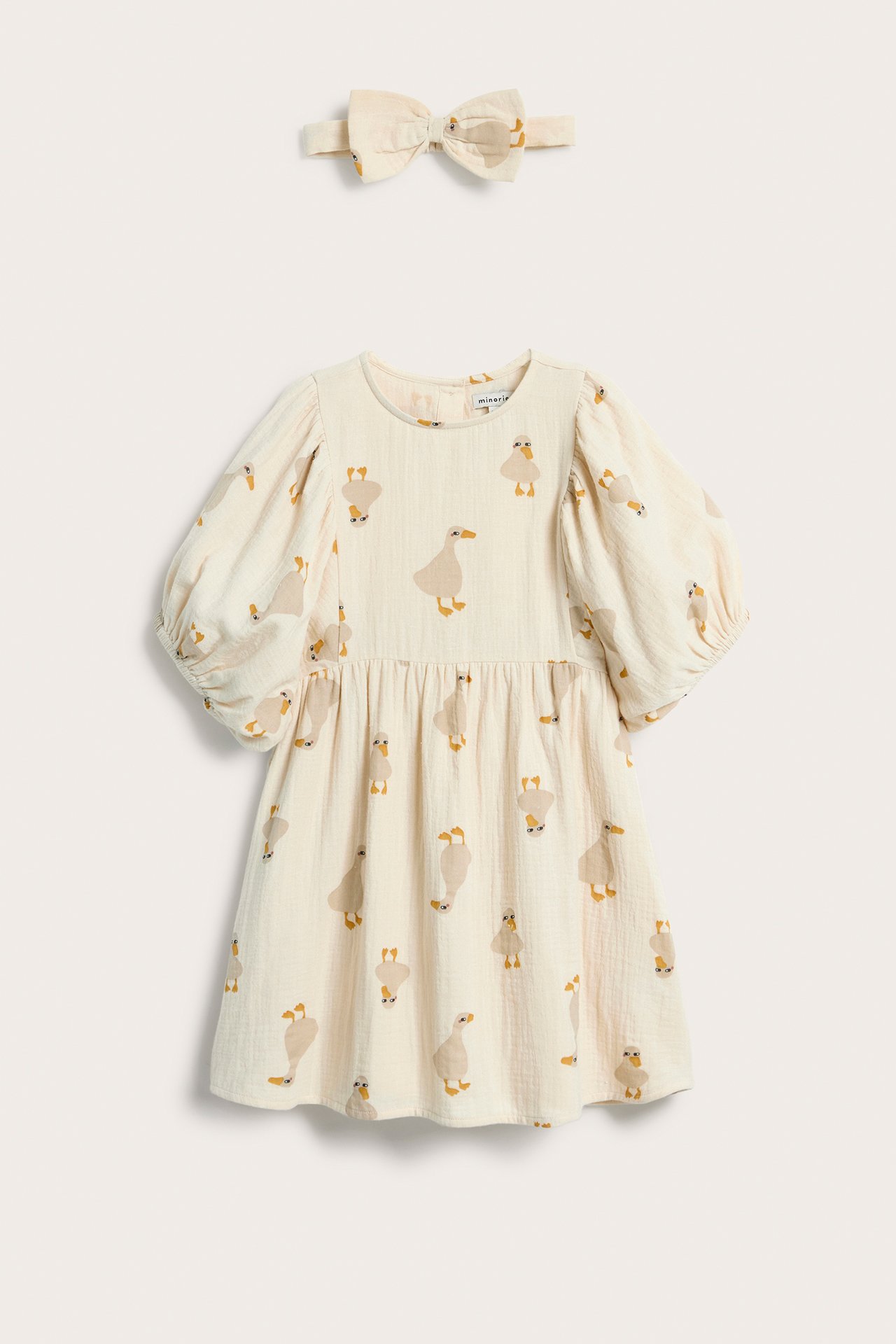 Framsida av en beige muslinklänning för barn med ankprint, puffärmar och matchande hårrosett.