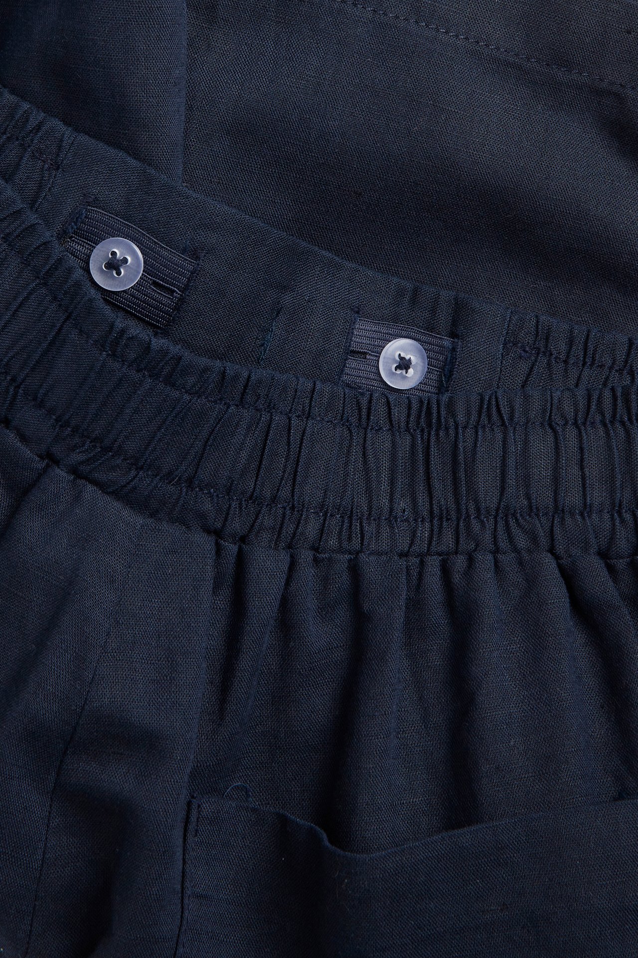 Nærbilde av mørkeblå linblandingsshorts med elastisk midje og innvendige justerbare knapper.