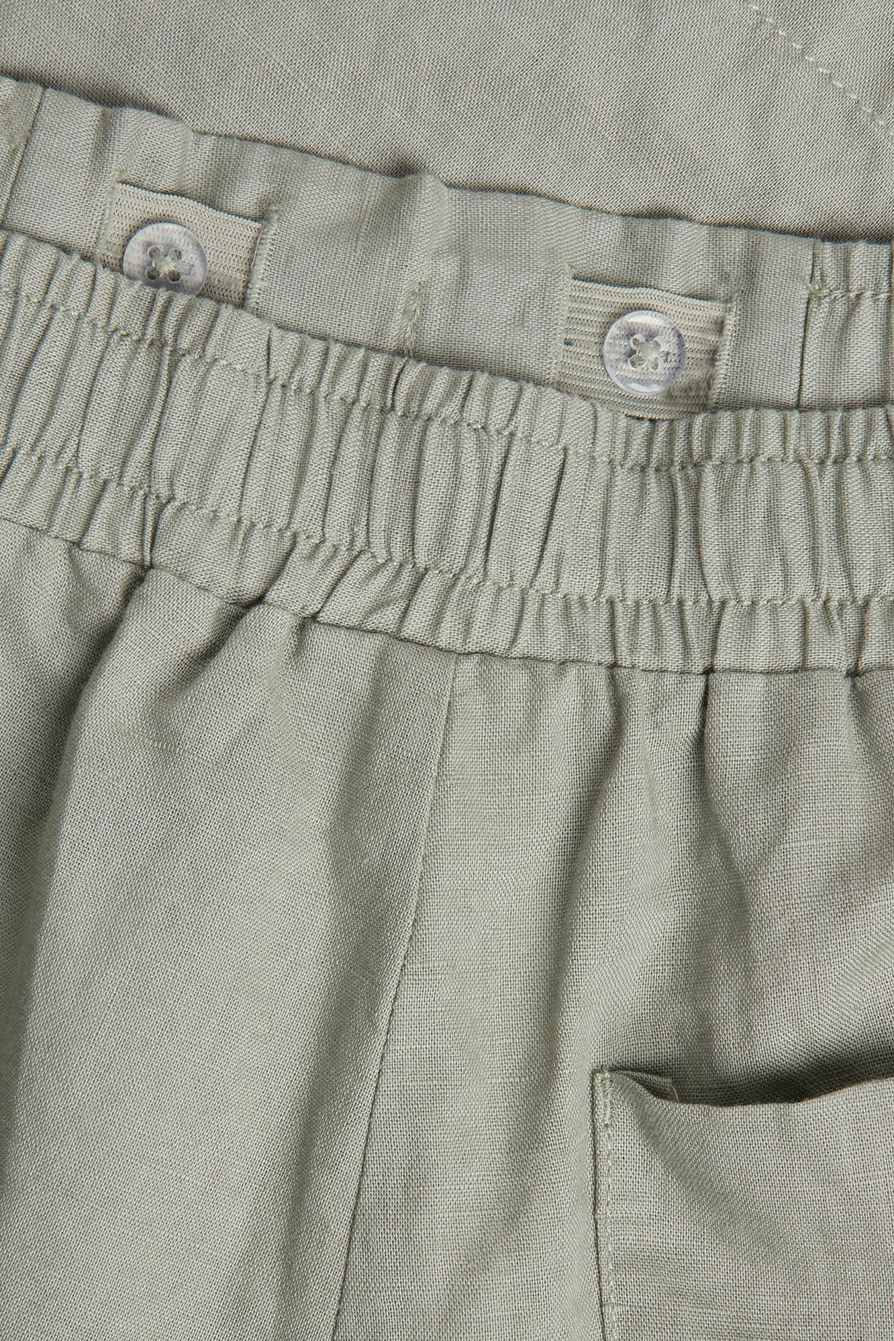 Närbild på ljusgröna shorts i linnemix med resår i midjan och justerbara innerknappar.