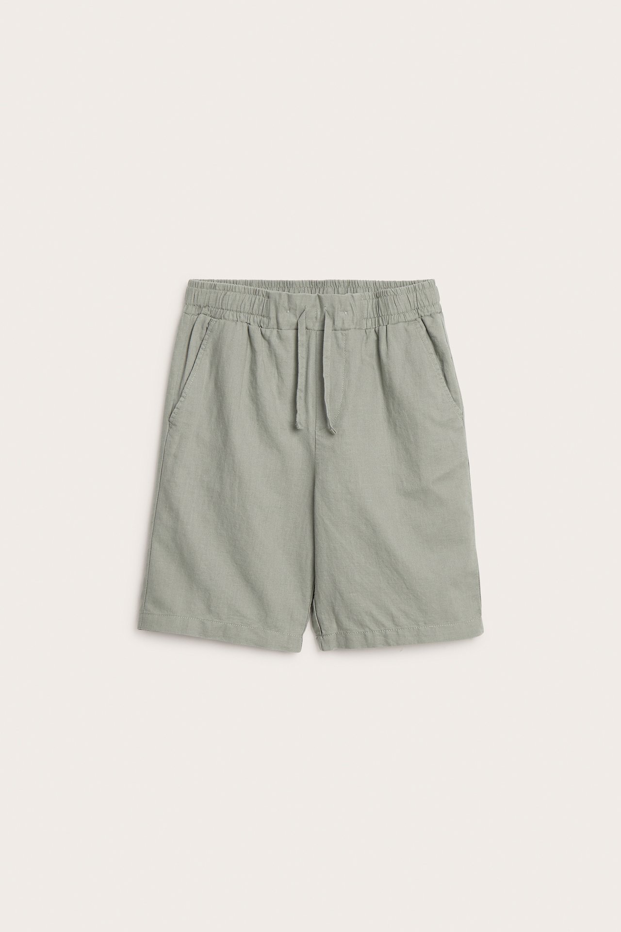 Framifrån, barnens gröna linneblandningsshorts med resår i midjan, dragsko och sidofickor.