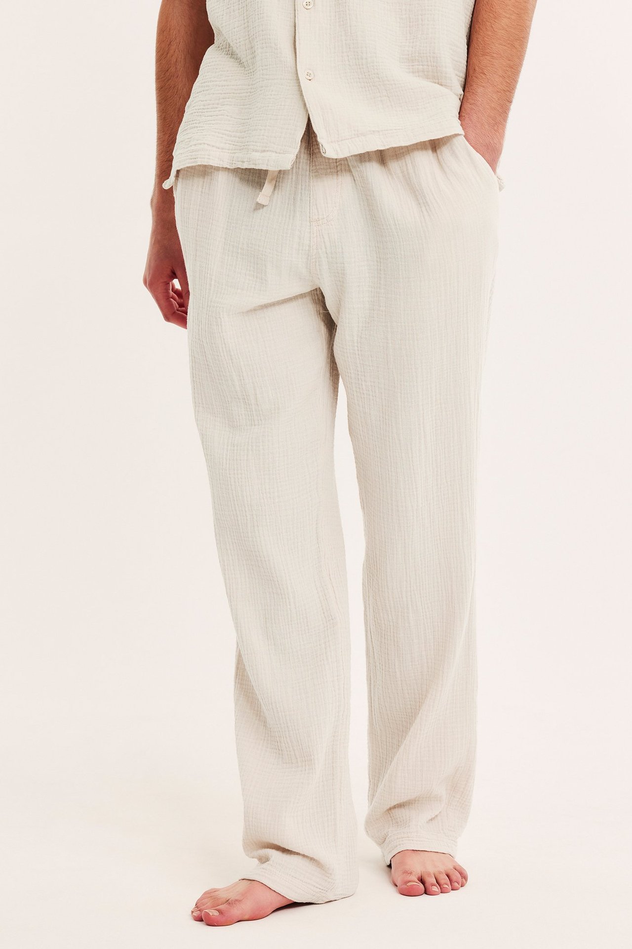 Framifrån, man bär ljusbeige pyjamasbyxor i bomullskrepp med matchande skjorta.