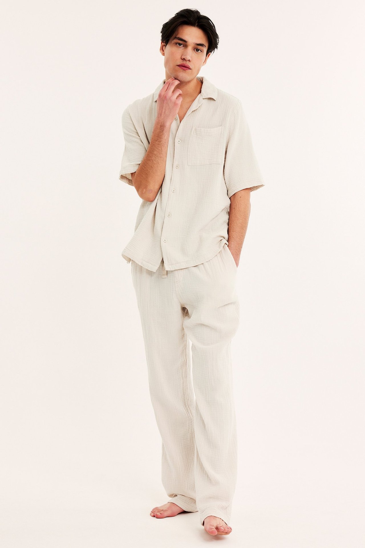 Framifrån, man i ljusbeige pyjamasbyxor i bomullskrepp med matchande kortärmad skjorta.