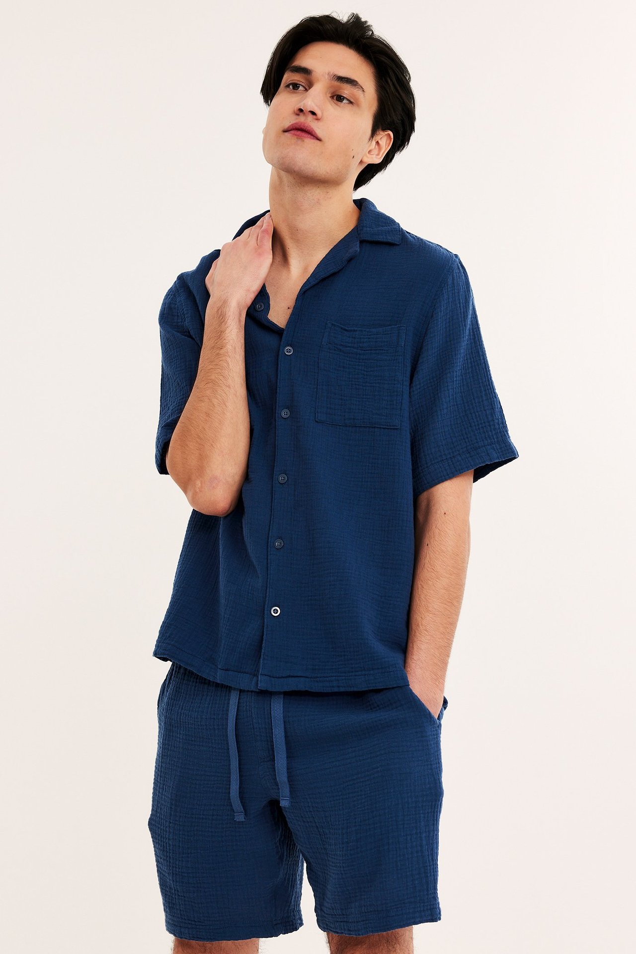 Edestä näkymä miehestä tummansinisessä kuvioidussa puuvillaisessa lyhythihaisessa pyjamapaidassa ja shortseissa.