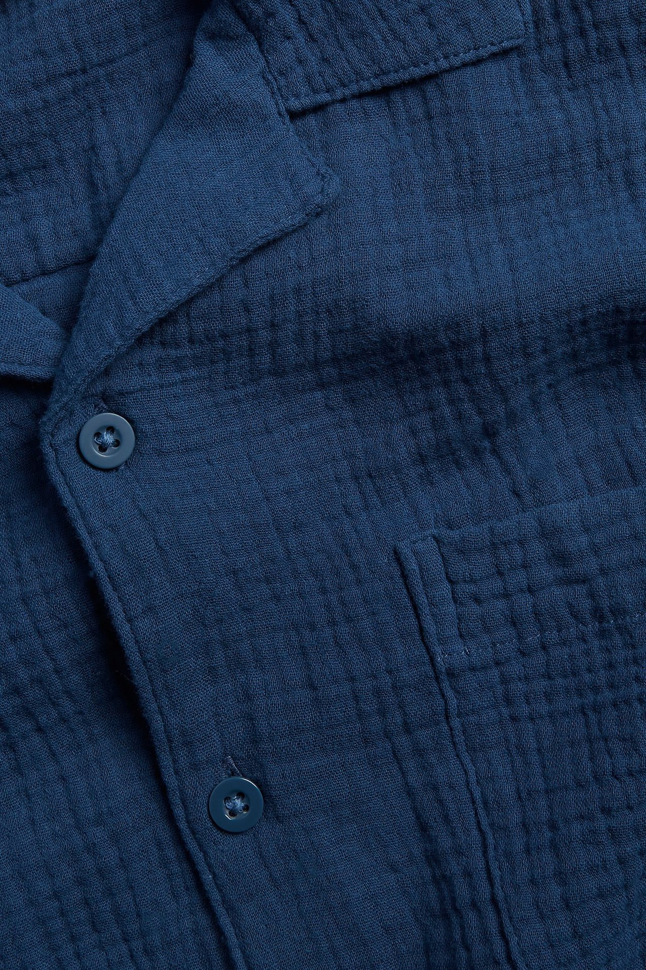 Zbliżenie na ciemnoniebieską męską bawełnianą koszulę piżamową z kołnierzykiem, guzikami i kieszenią na piersi.