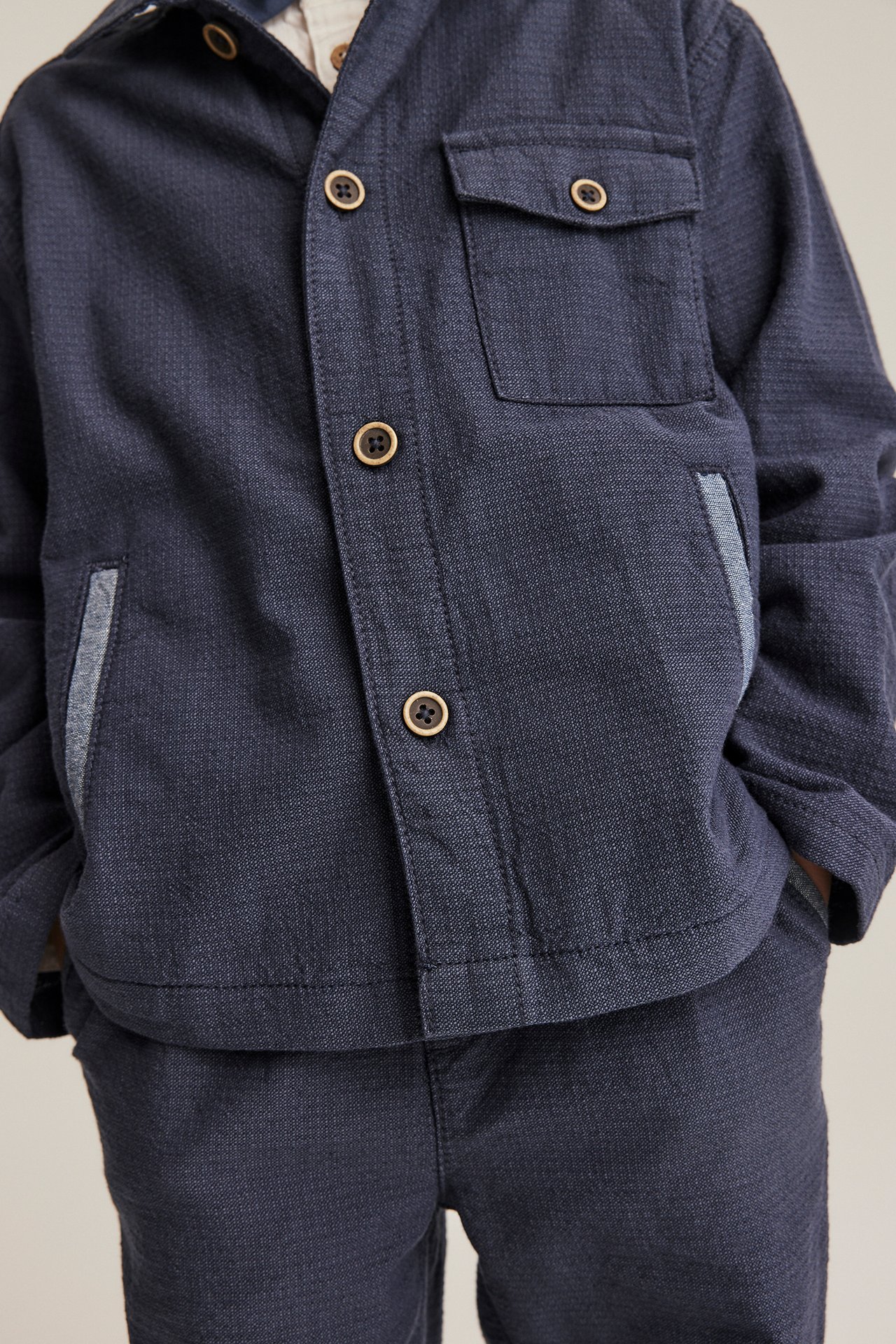 Barns mørkeblå chambray-overshirt med treknapper, brystlomme og matchende bukser, forfra.