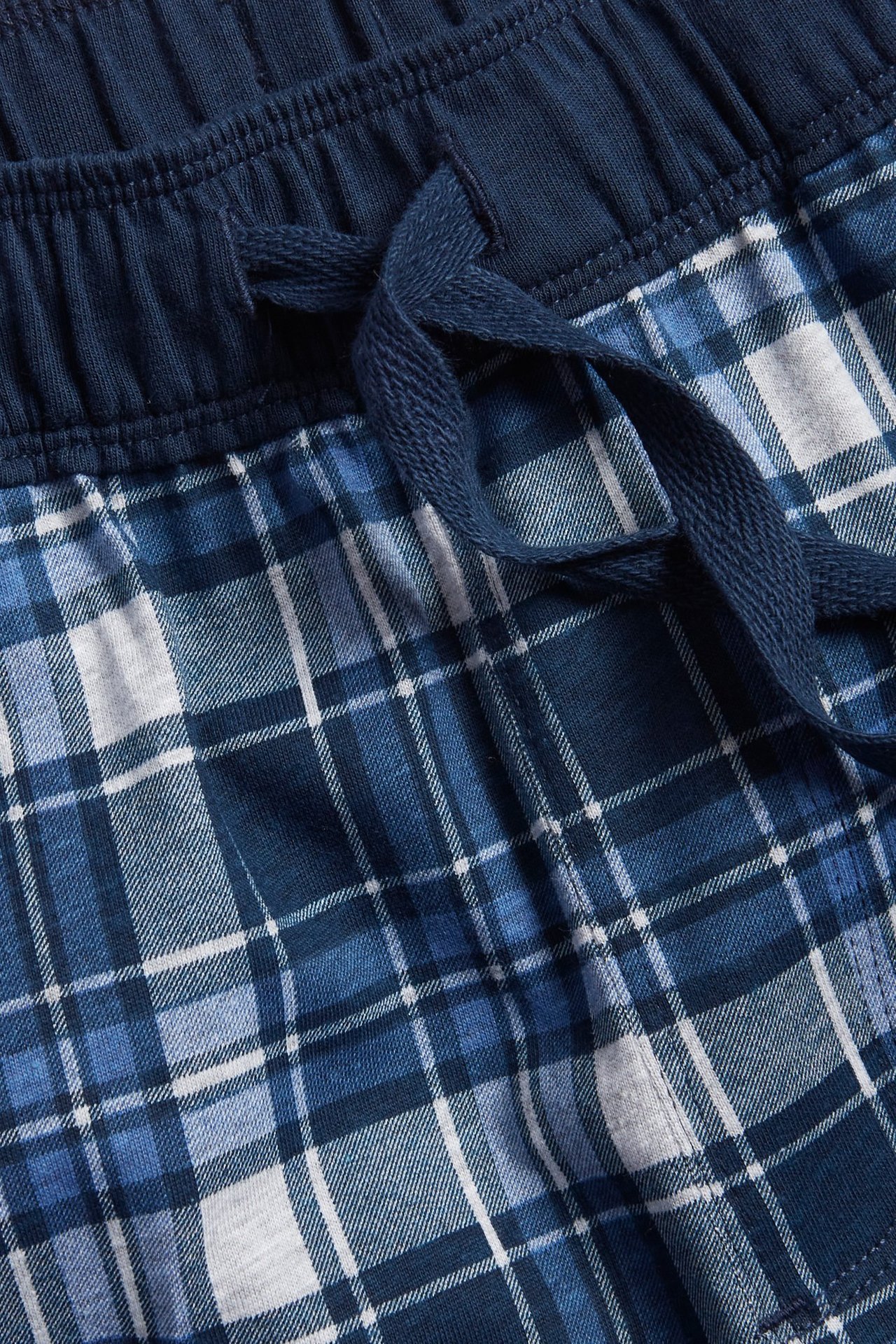 Zbliżenie na granatowe i białe piżamowe spodnie w kratę z dżerseju z granatowym sznurkiem w pasie.
