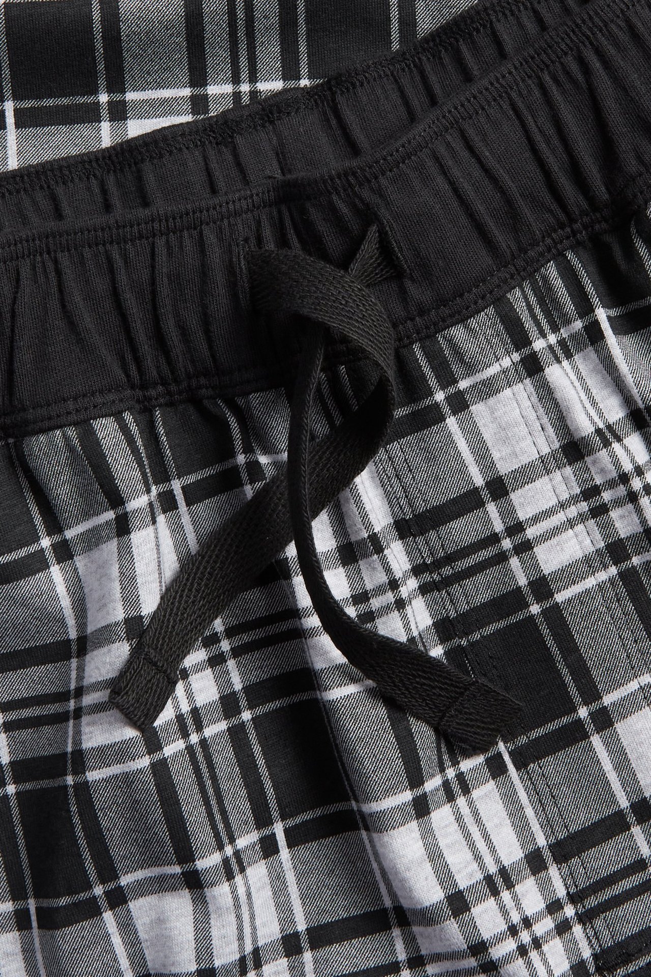 Lähikuva mustavalkoisista ruudullisista jersey-pyjamahousuista, joissa musta joustava vyötärönauha ja kiristysnyöri.