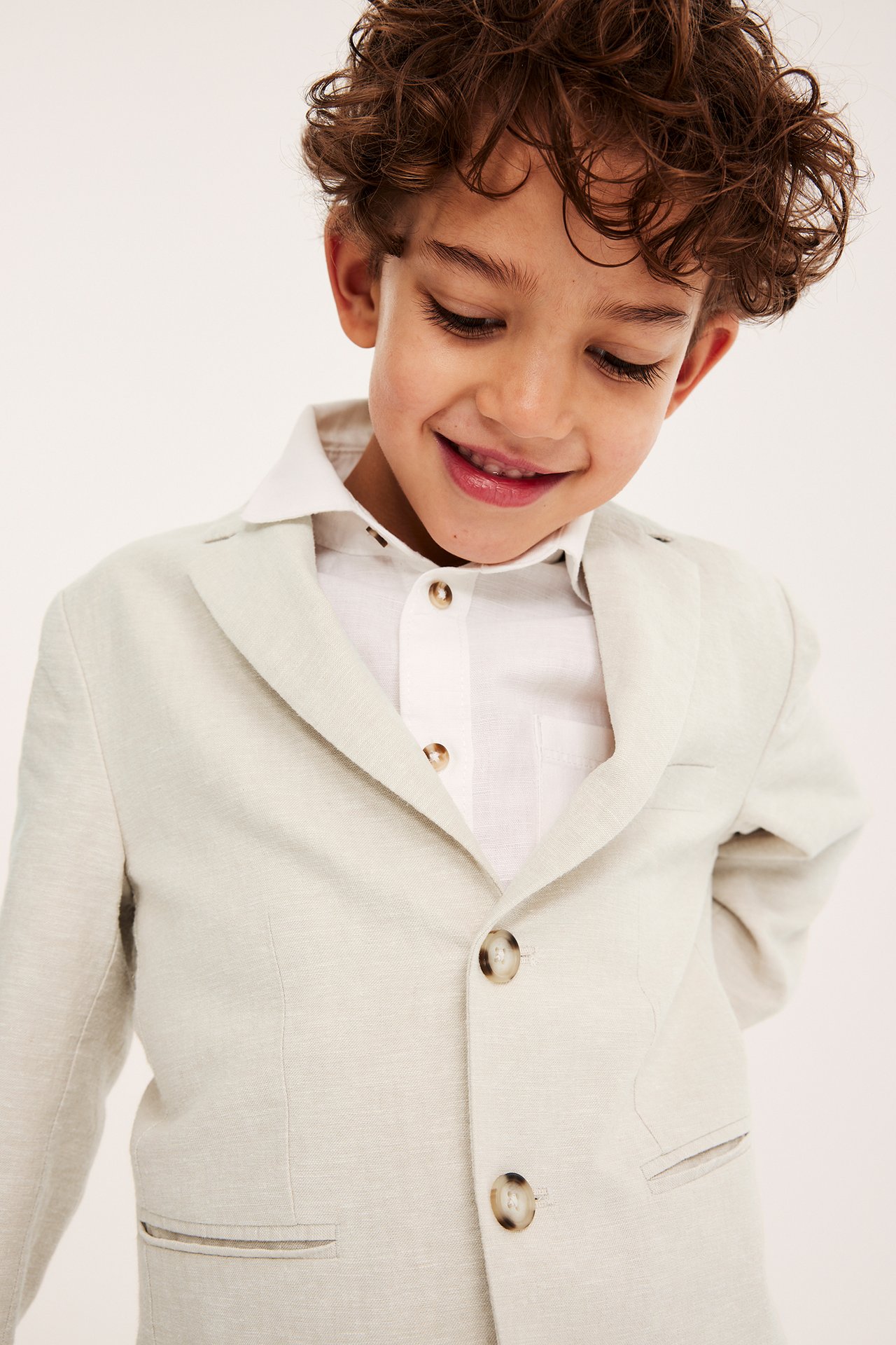 Frontbilde av et smilende barn i en lys beige linblanding blazer over en hvit skjorte.