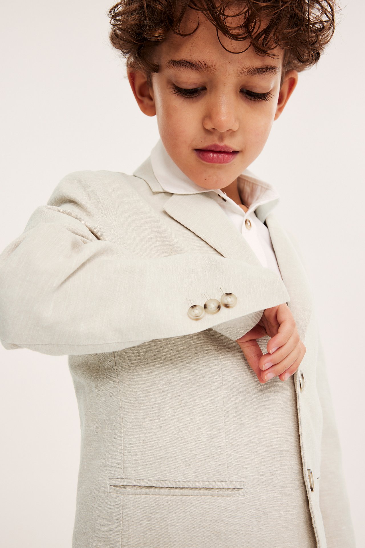 Nærbilde av et barn i en lys beige linblanding blazer over en hvit pikétrøye.