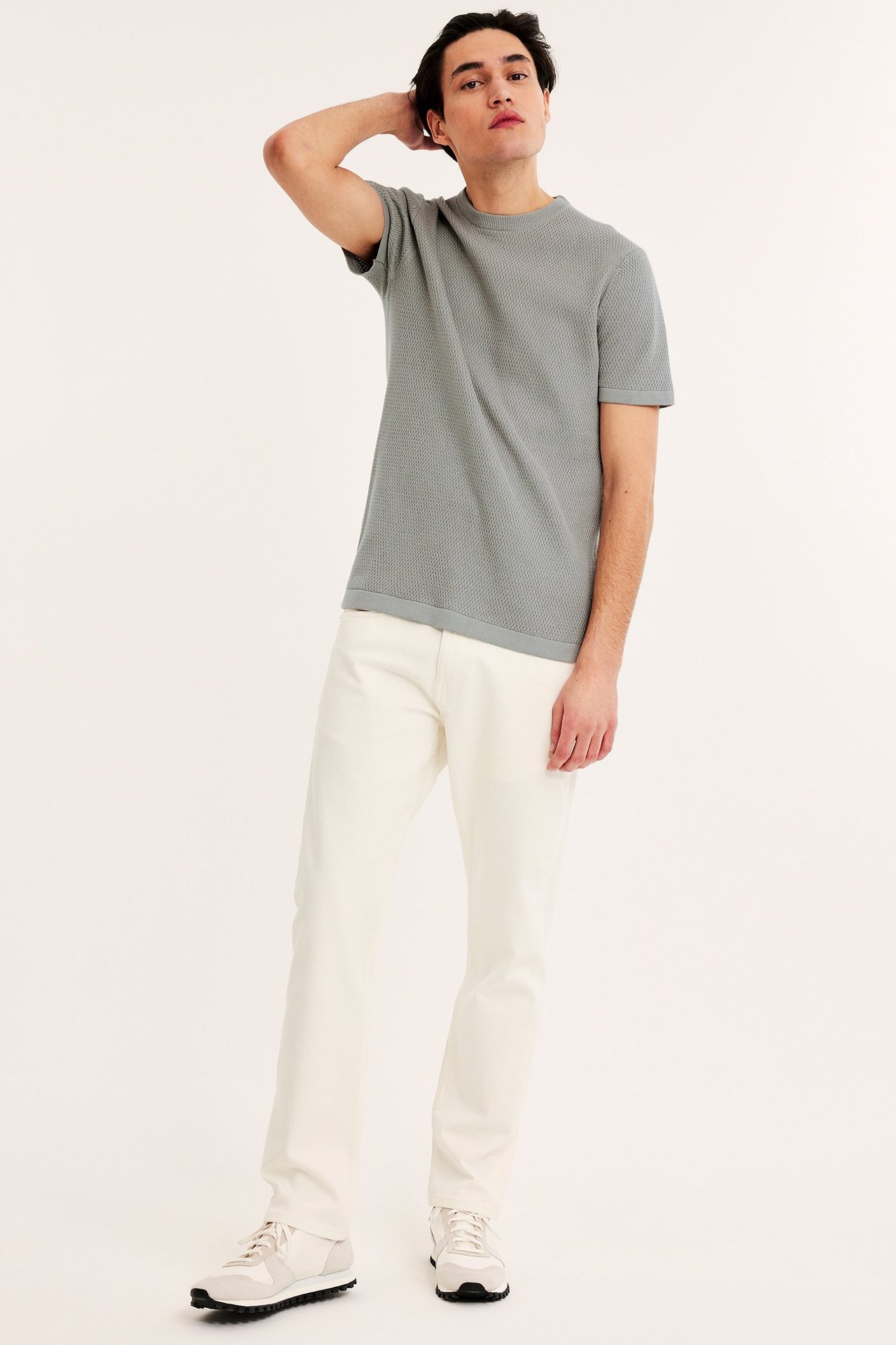 Frontvy av en man i ljusgrön kortärmad stickad tröja med struktur, krämfärgade byxor och sneakers.