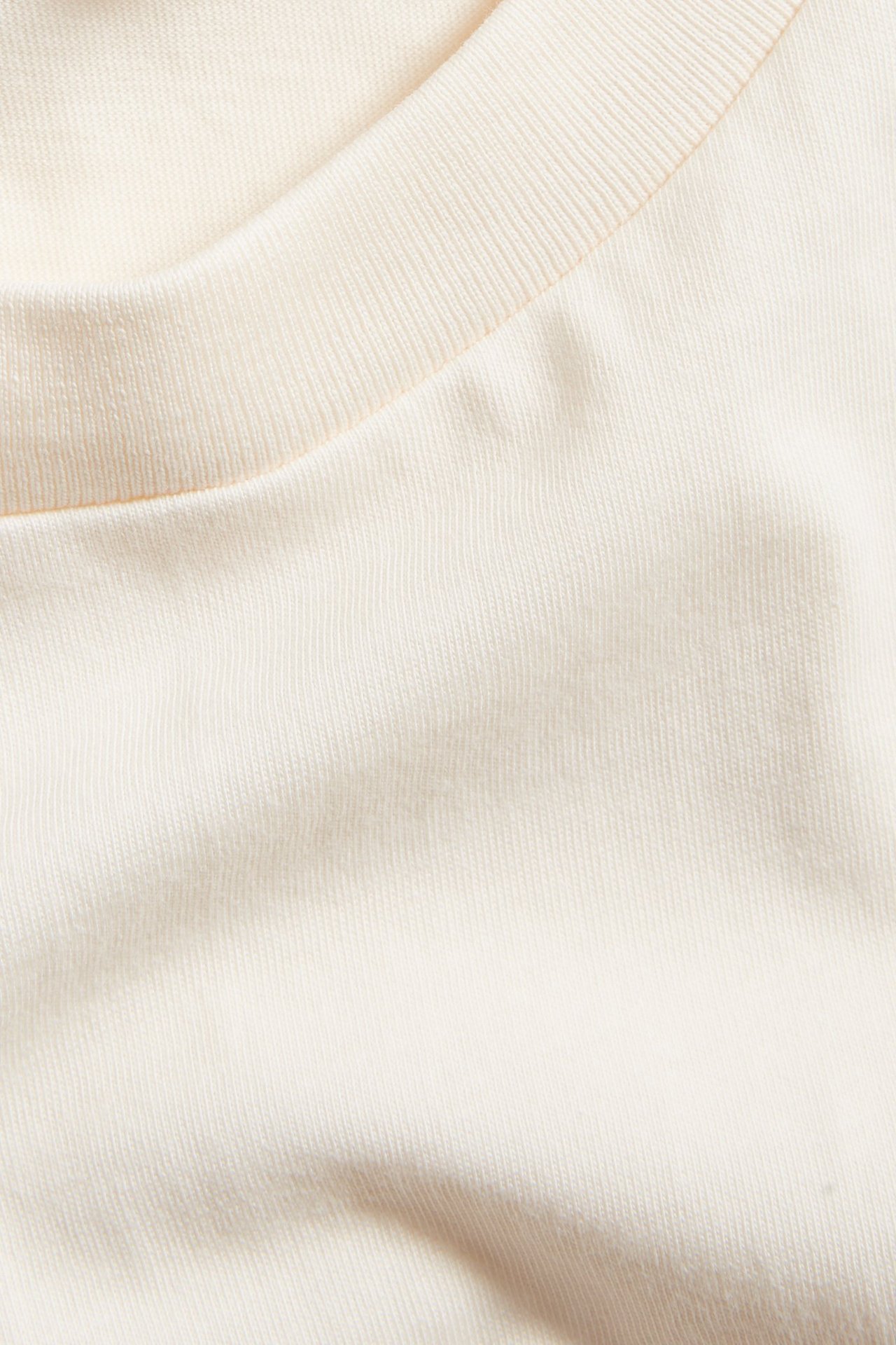 Zbliżenie na kremowy, oversize'owy bawełniany T-shirt z prążkowanym dekoltem.