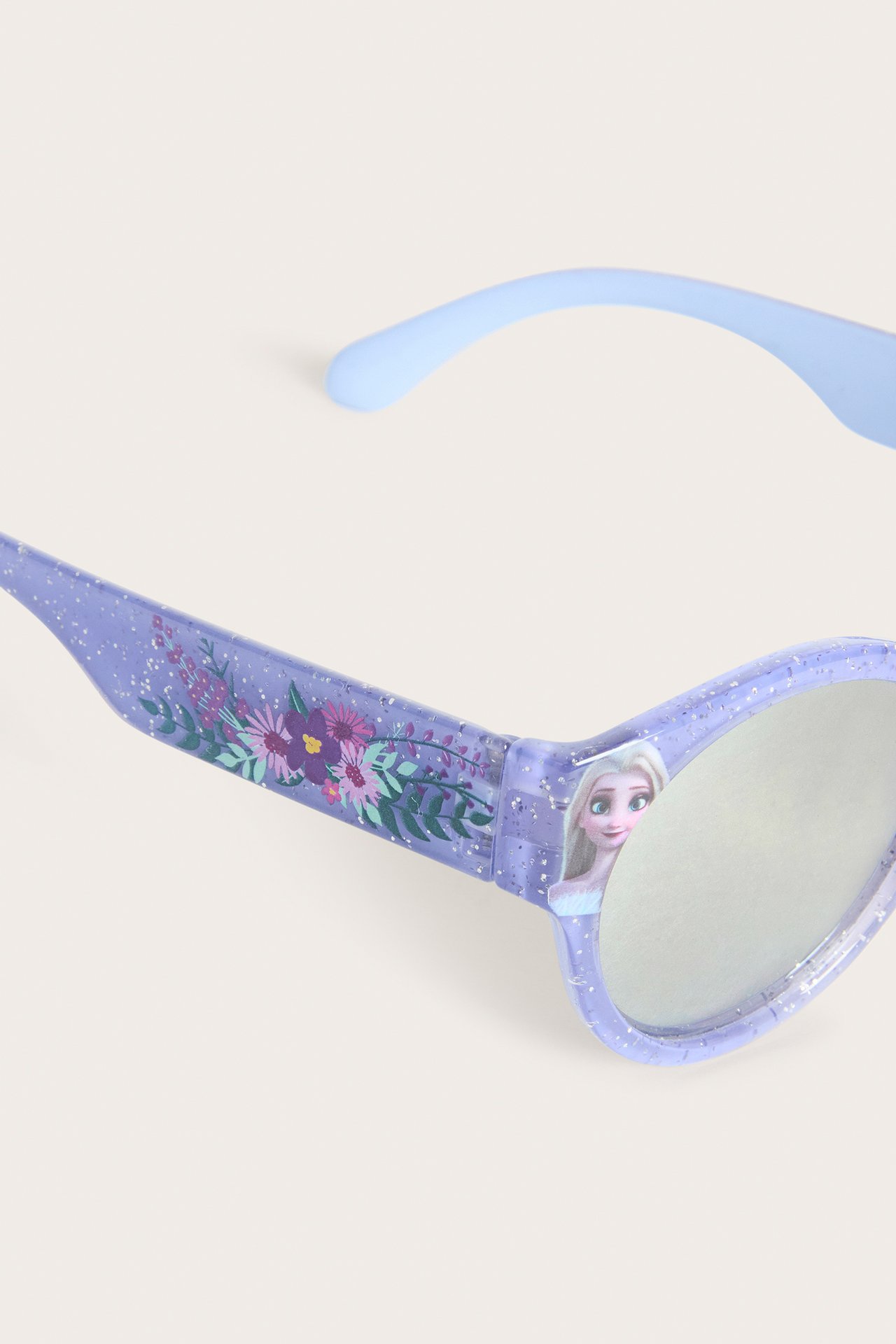 Närbild på glittriga lila barnsolglasögon med spegelglas, blommigt tryck och Elsa-motiv.