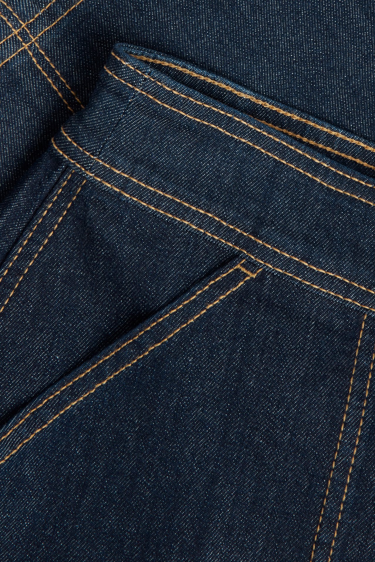 Lähikuva tummasta denim-kietaisuhameesta, näyttäen oranssit tikkaukset ja kankaan tekstuurin.