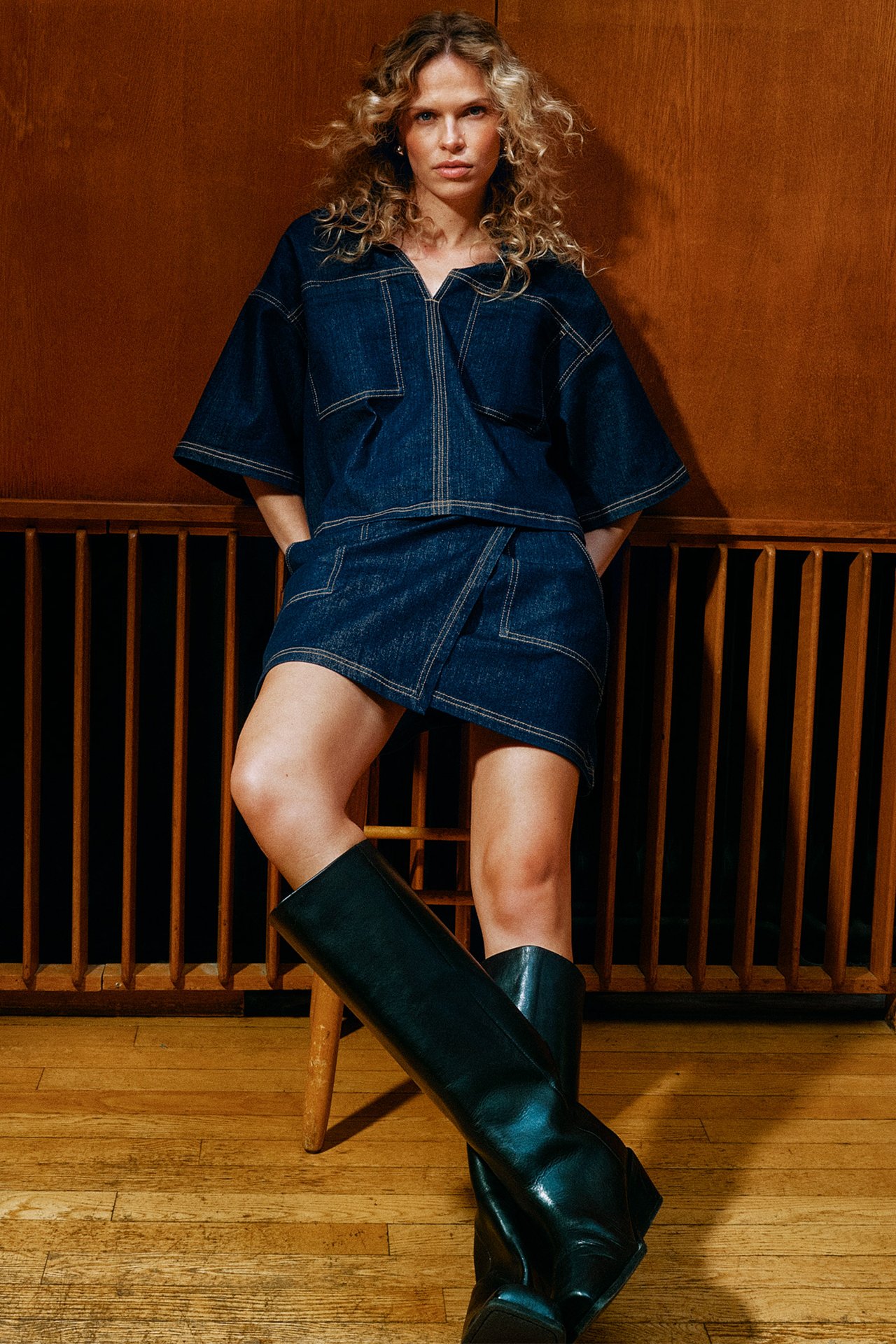 Etunäkymä: Nainen tummassa denim-kietaisuhameessa, jossa taskut, yhteensopiva toppi ja tummat polvisaappaat.