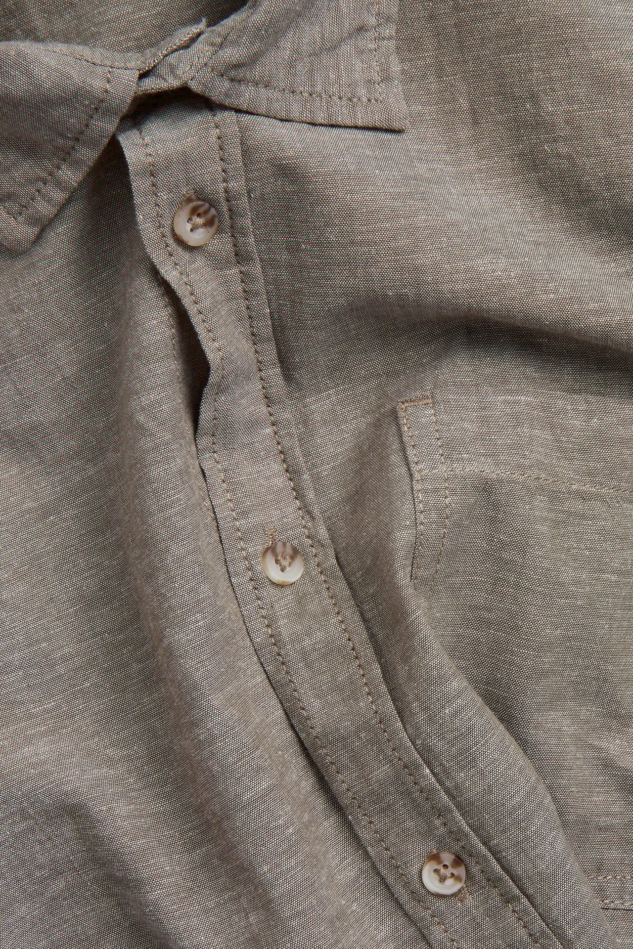 Zbliżenie na zieloną koszulę z krótkim rękawem z bawełny i lnu, z guzikami, kołnierzem i kieszenią.