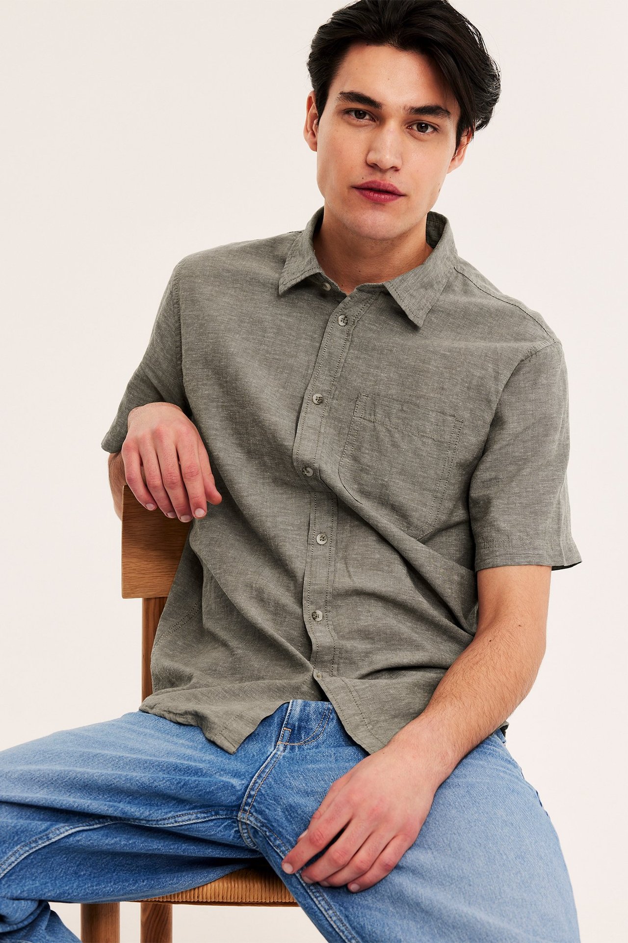Forfra, mann i grønn kortermet linskjorte med knapper og blå jeans.