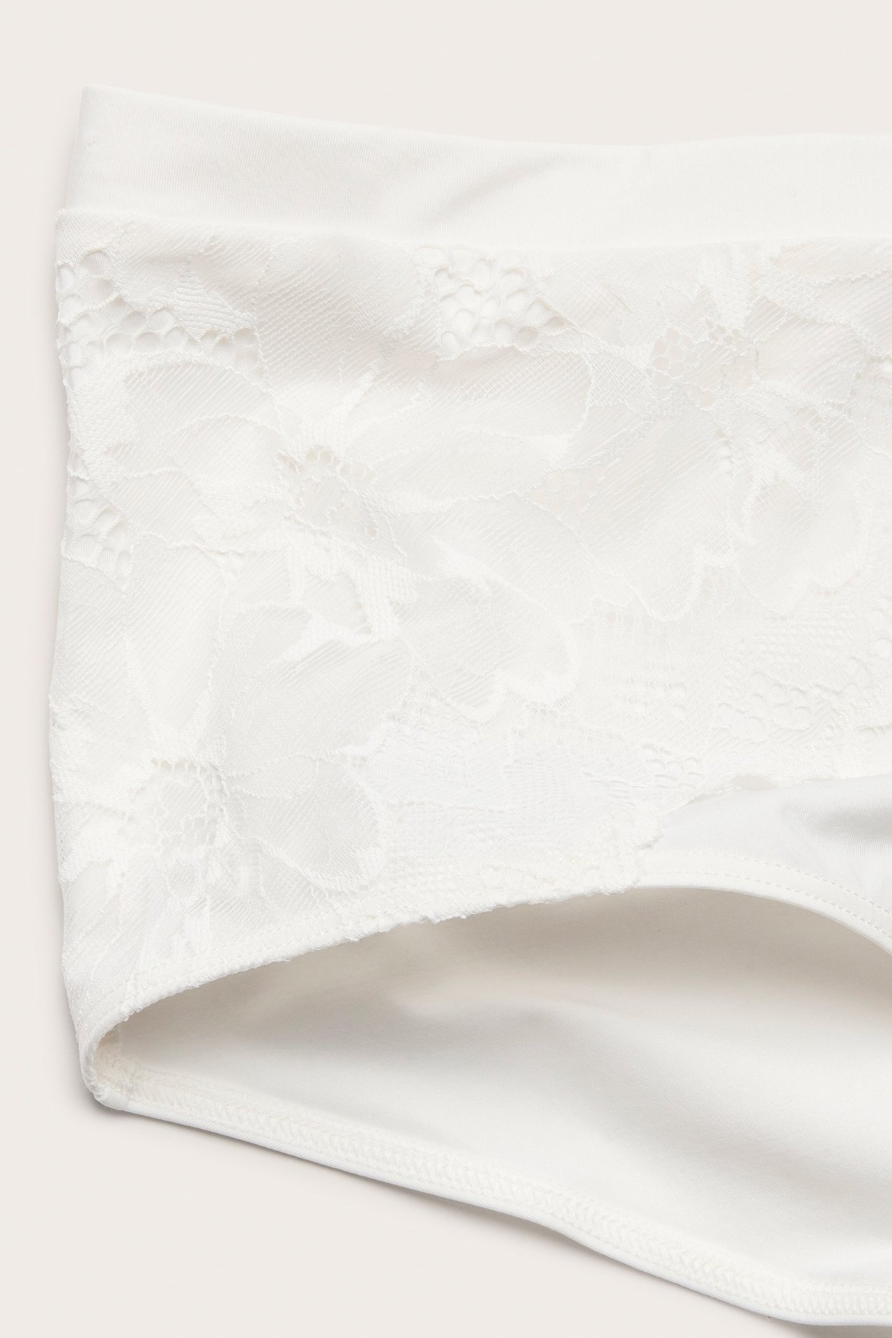 Zbliżenie białych fig typu hipster z szerokim koronkowym pasem w kwiaty i gładkim mikrowłóknem.