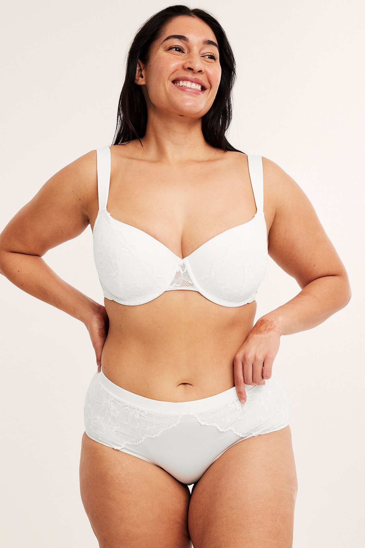 Frontbilde av en smilende kvinne i hvite blonde-hipstertruser og matchende hvit blonde-BH.