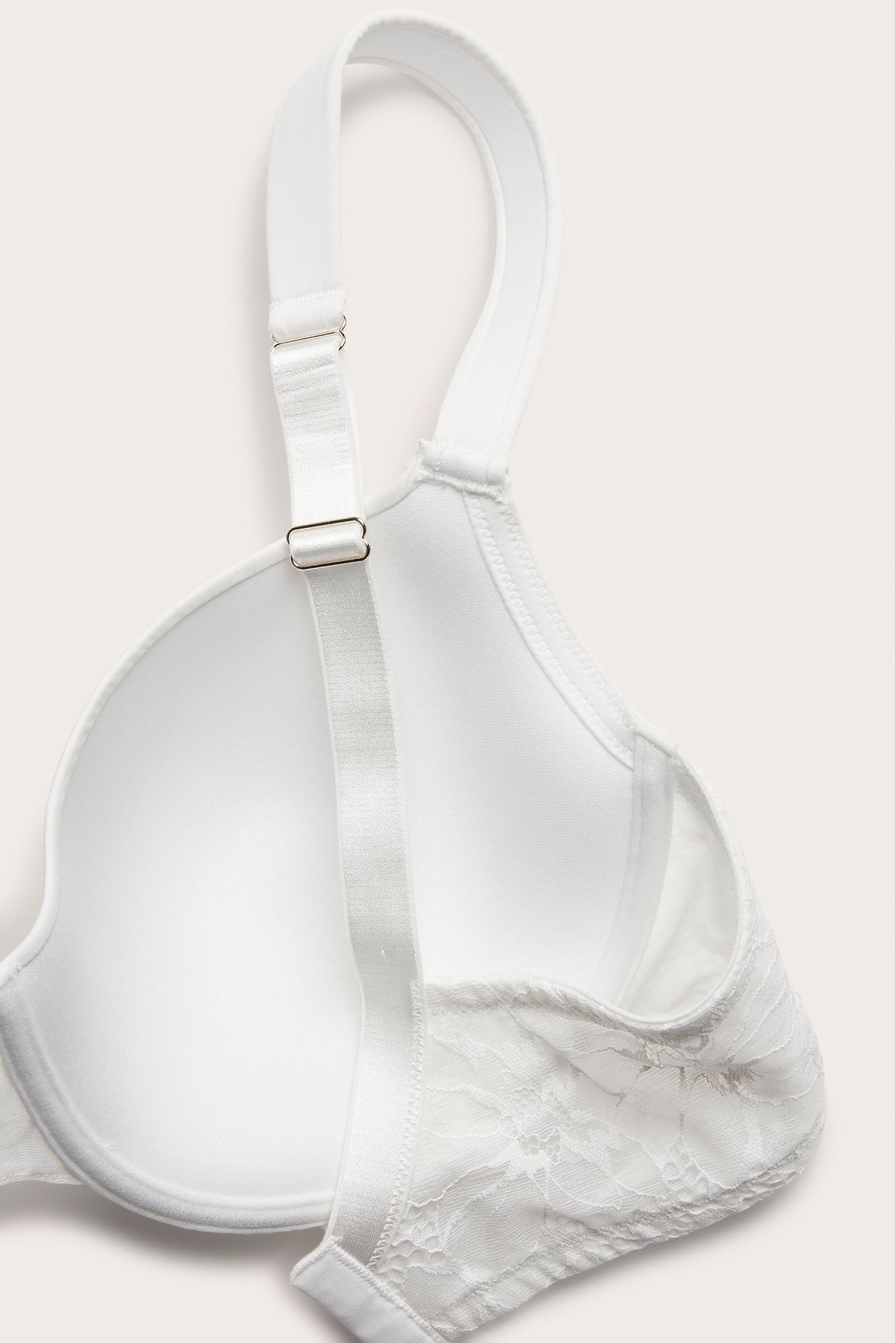 Närbild, uppifrån, av en vit vadderad spets-bh med bygel och justerbara axelband.