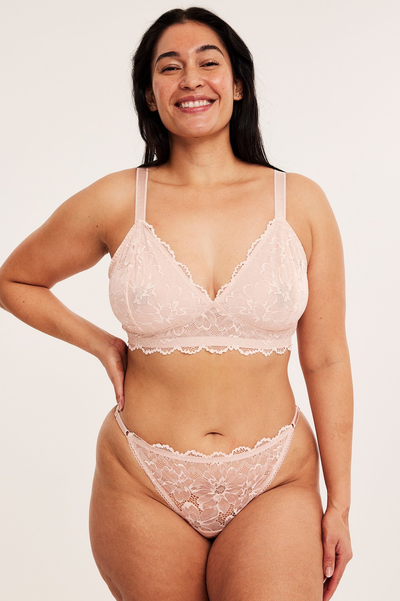 Frontbilde: kvinne i lys rosa blondestringtruse med justerbare sidebånd og matchende blondebralette.