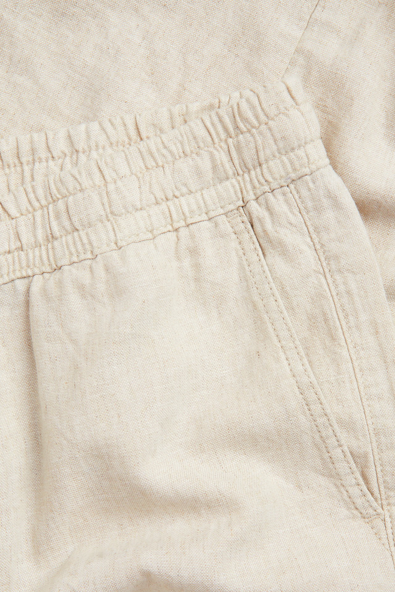 Nærbilde av herrebukser i beige linblanding med elastisk linning og sidelomme.