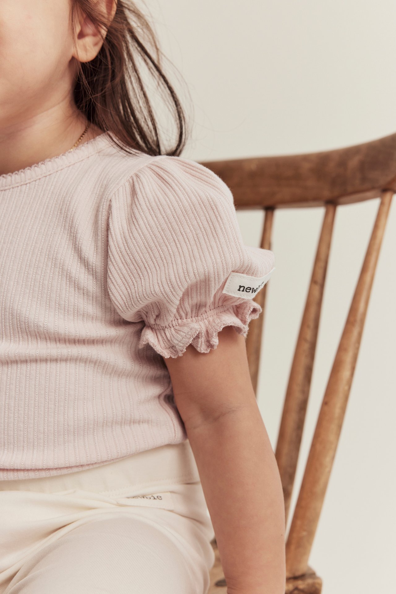 Närbild sidovy av ett barn i ljusrosa ribbad body med puffärm och ljusa byxor.