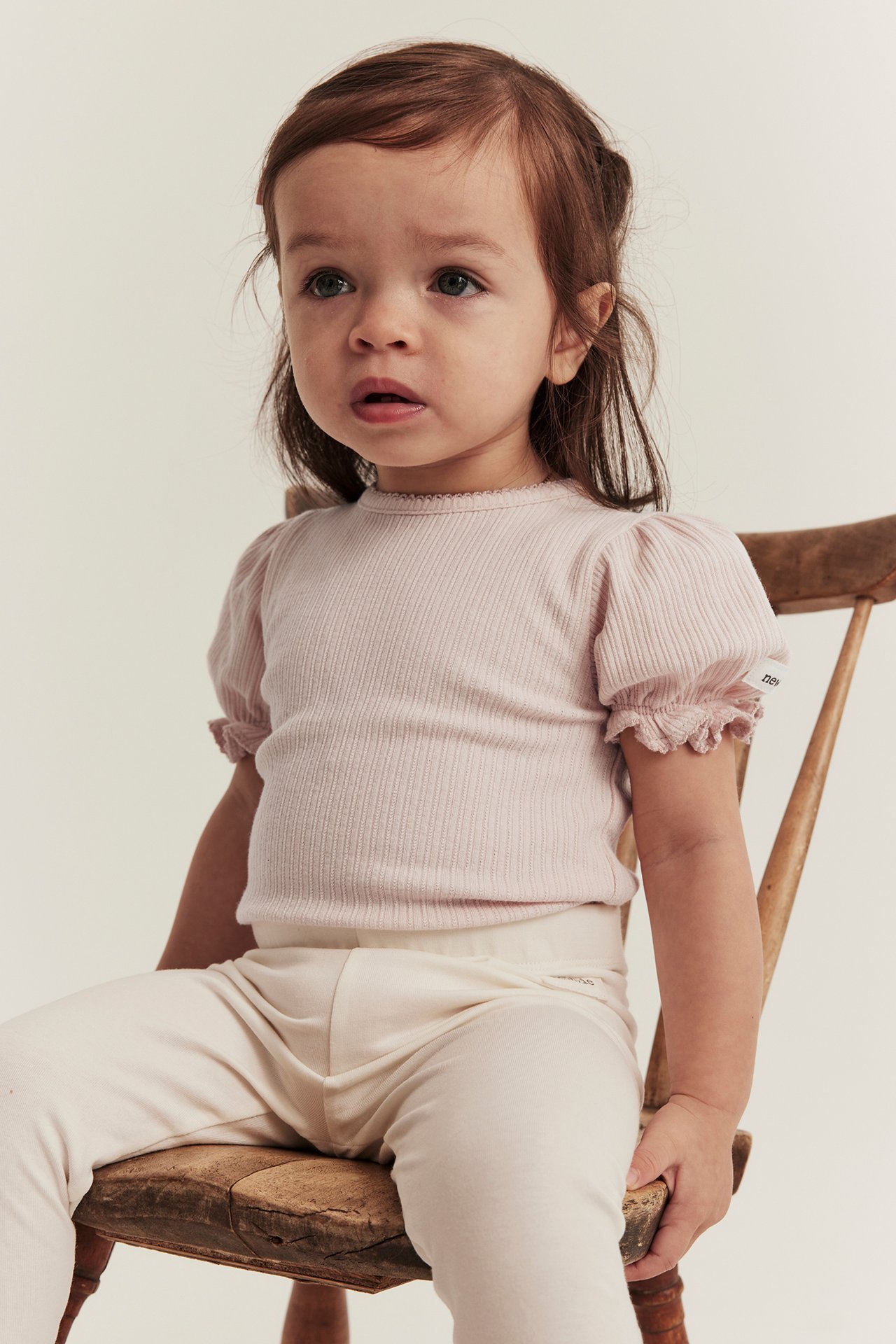 Framifrån: baby i ljusrosa ribbad jerseybody med puffärm och benvita leggings.
