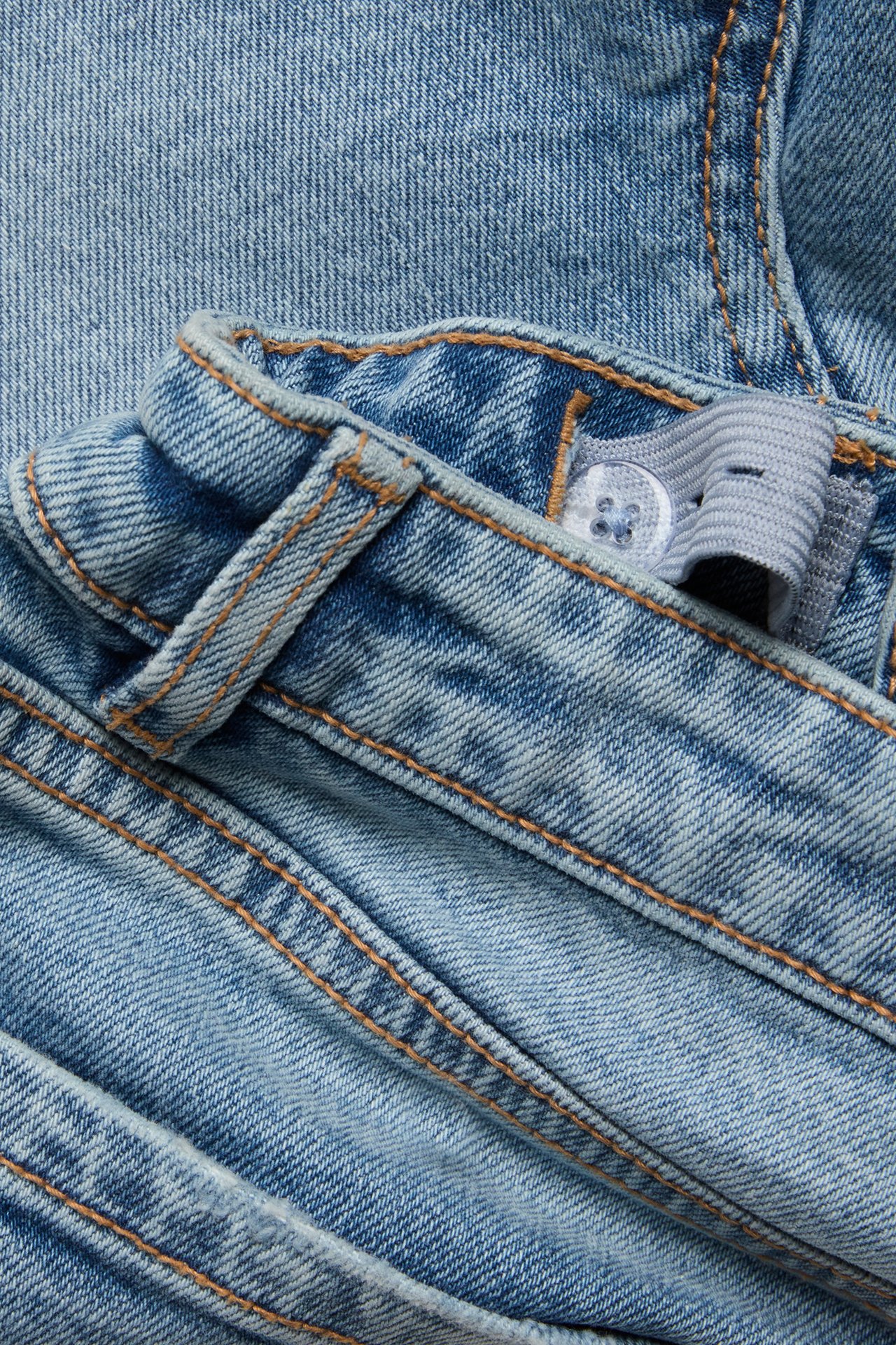 Närbild av ljusblå jeansshorts med bruna sömmar och justerbar resår i midjan med knapp.