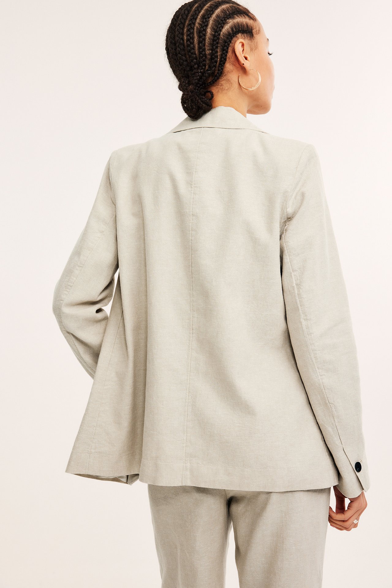 Ryggvisning av en kvinne i en offwhite melert linblanding-blazer og matchende bukser, med gullringer.