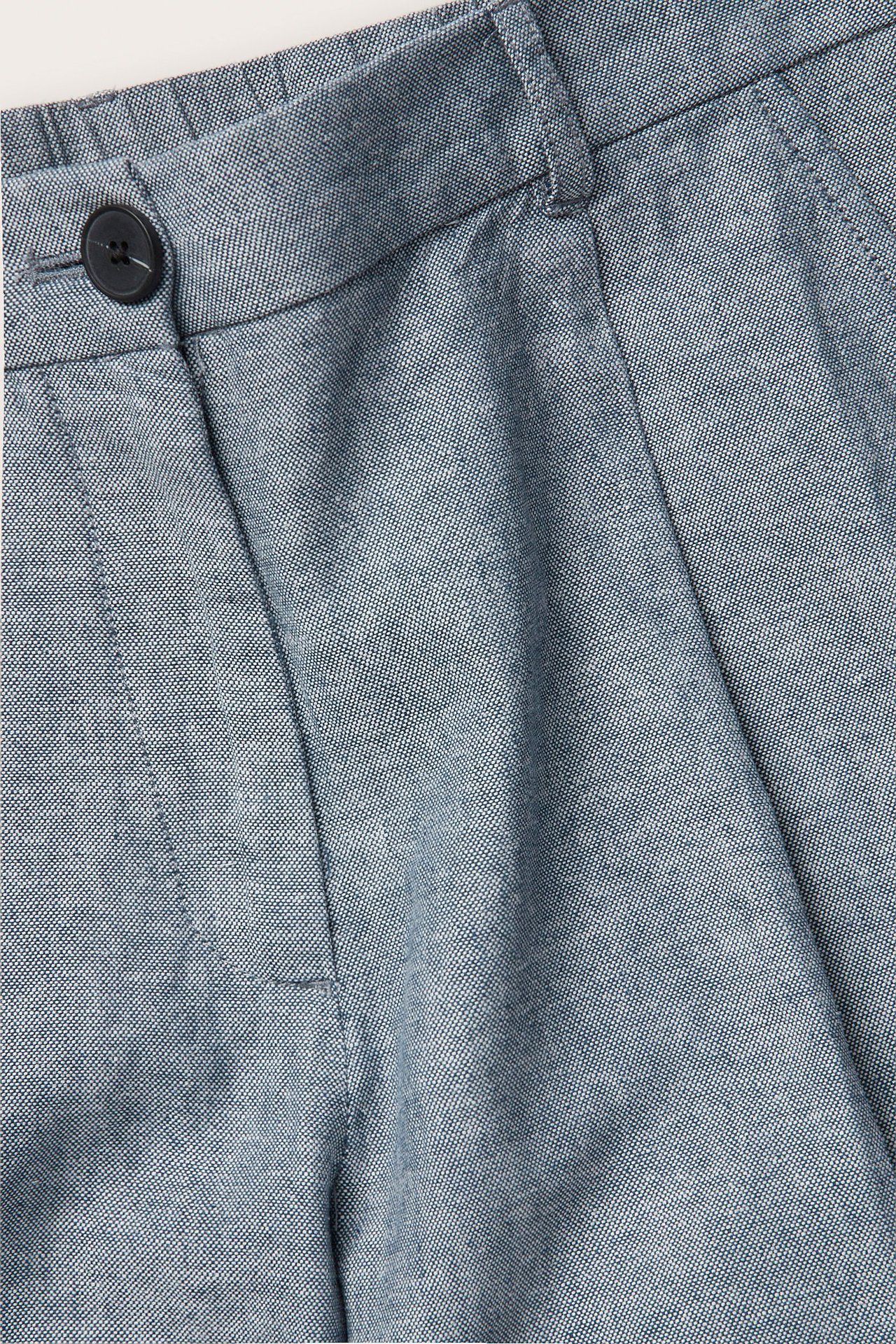 Zbliżenie na niebieskie melanżowe szorty z mieszanki lnu z czarnym guzikiem i zakładkami.