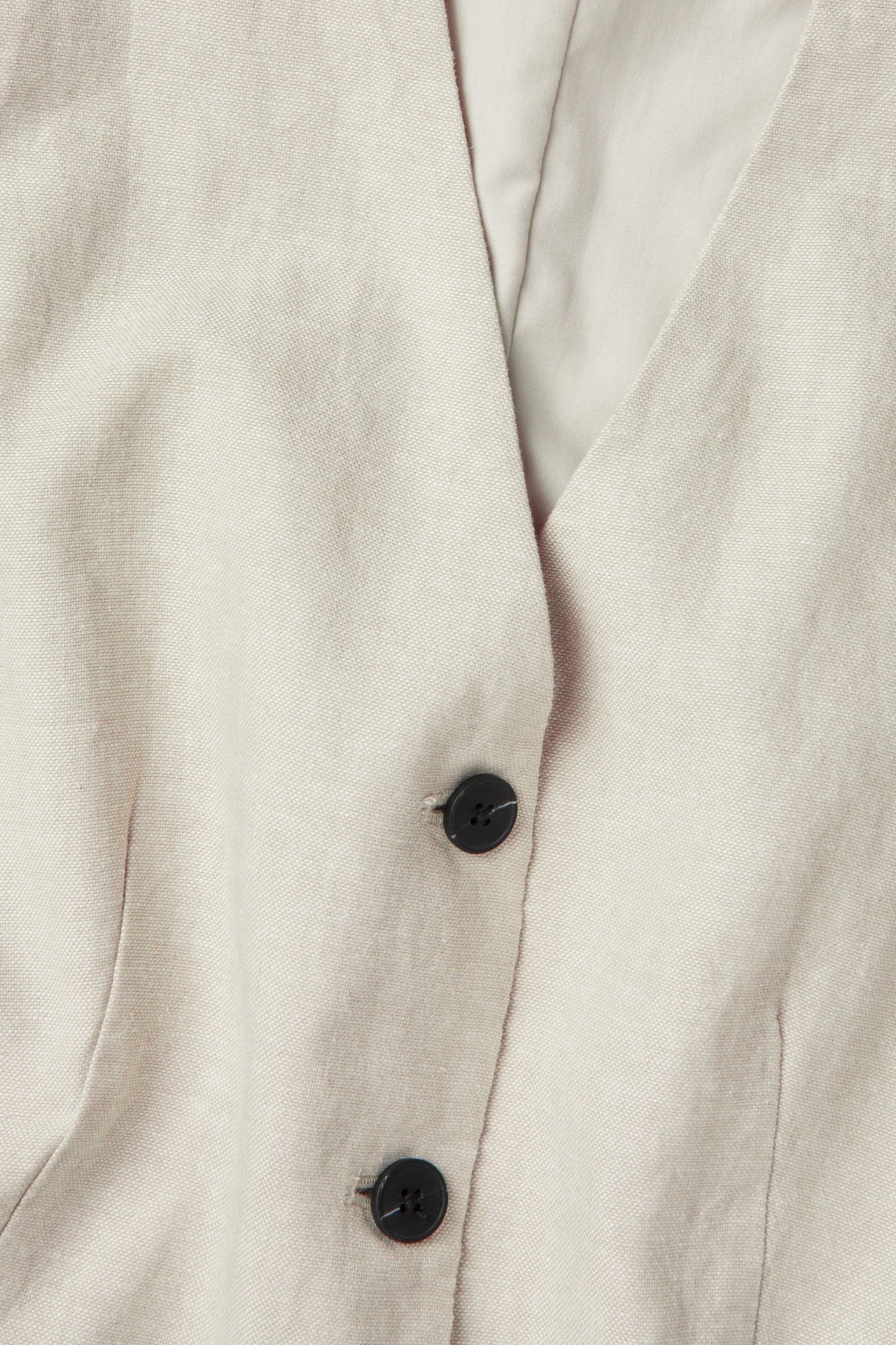 Zbliżenie na off-white melanżową kamizelkę z mieszanki lnu z dwoma czarnymi guzikami.