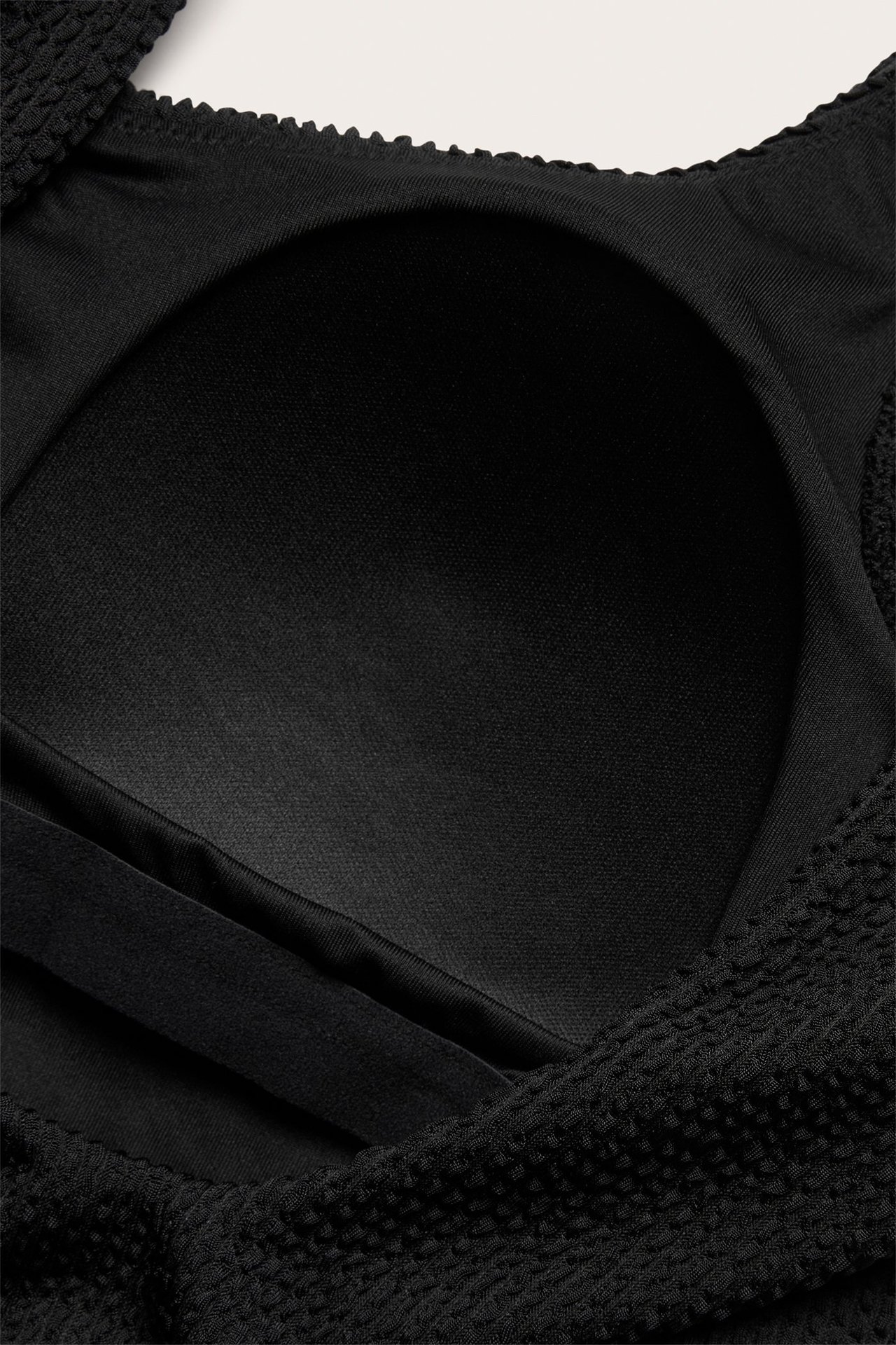 Zbliżenie czarnego, strukturalnego kostiumu kąpielowego z profilowaną miseczką i gładką podszewką.