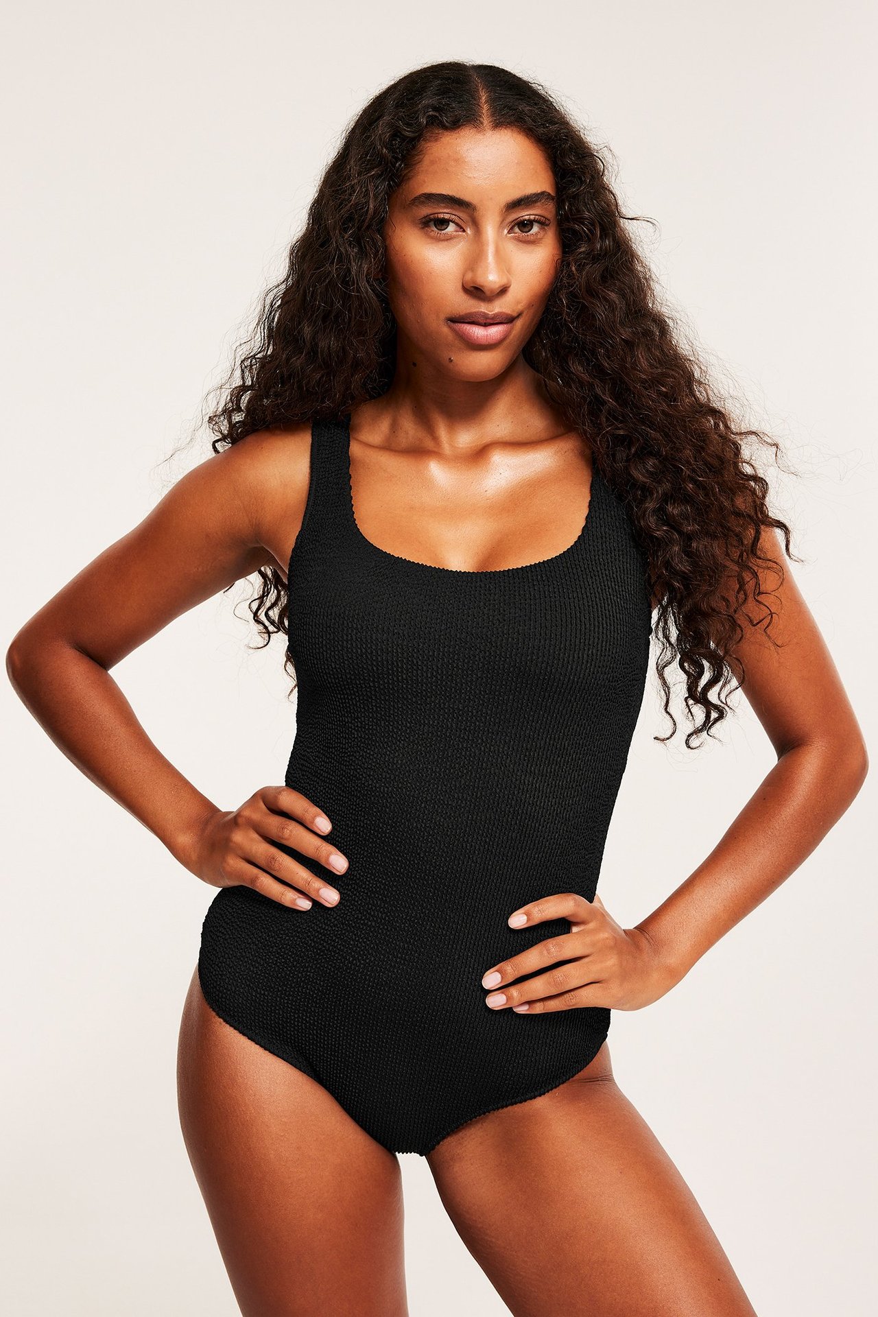 Widok z przodu kobiety w czarnym, teksturowanym jednoczęściowym stroju kąpielowym z okrągłym dekoltem.