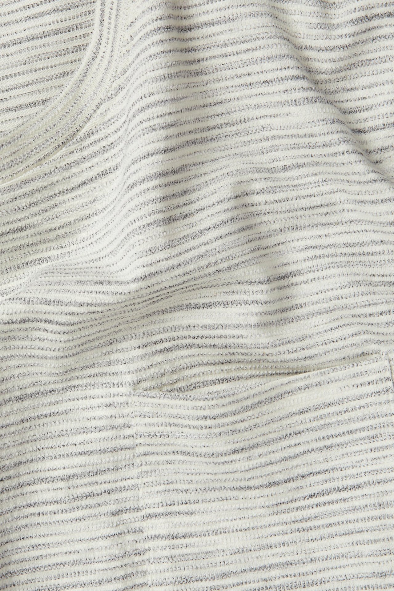 Zbliżenie na męski T-shirt w kolorze złamanej bieli, z melanżowej tkaniny strukturalnej, z dekoltem O i kieszenią.