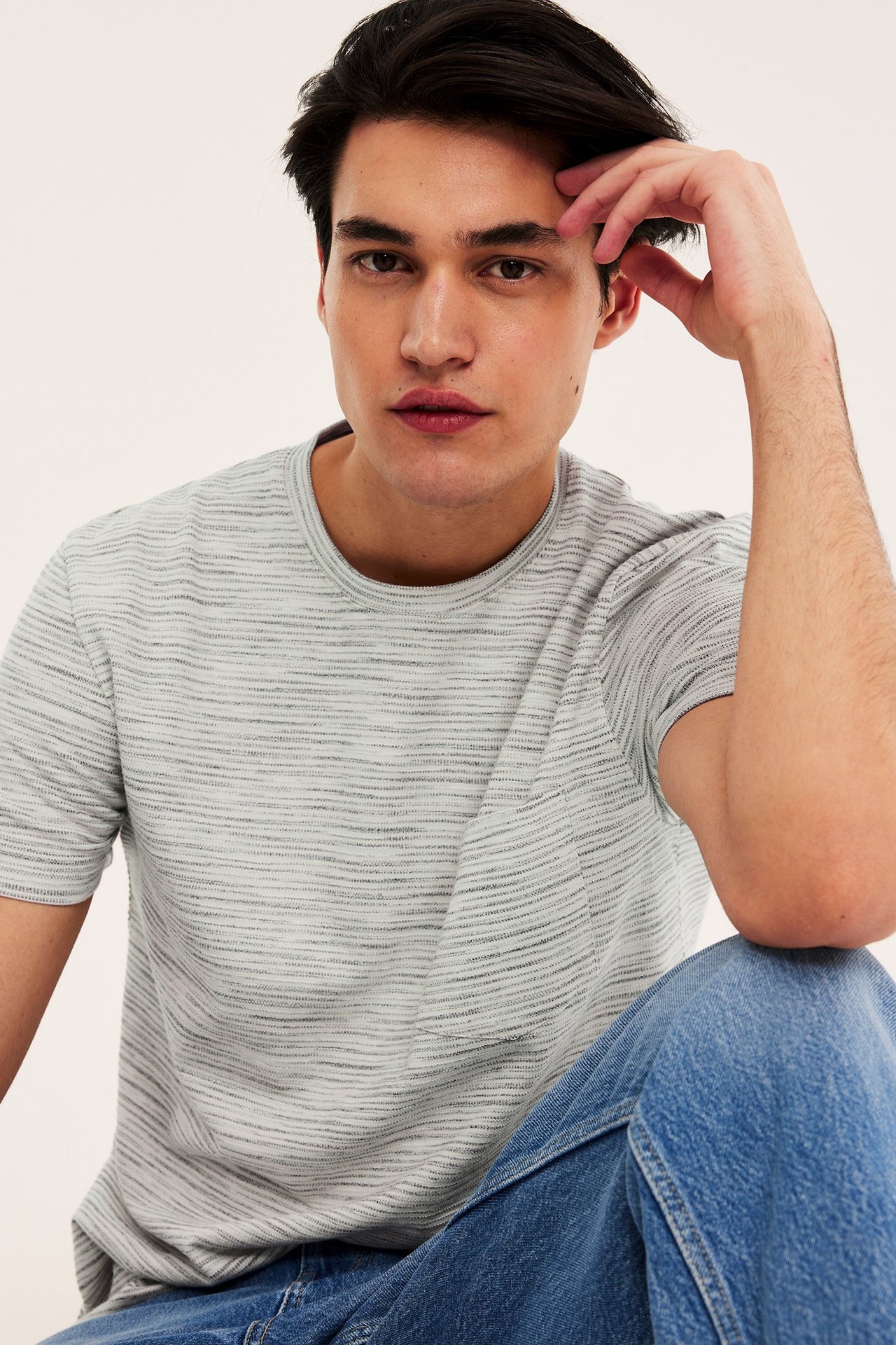 Mies luonnonvalkoisessa meleeratussa strukturoidussa O-aukko t-paidassa rintataskulla ja sinisissä farkuissa, edestä.