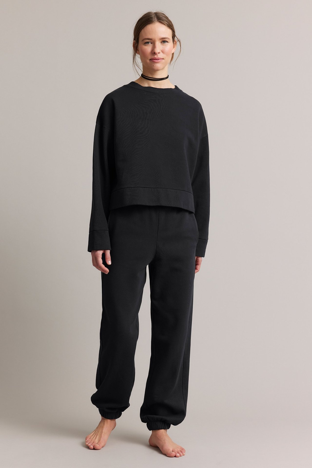 Forfra: kvinne i svart jerseygenser med vasket look og matchende svarte joggebukser.