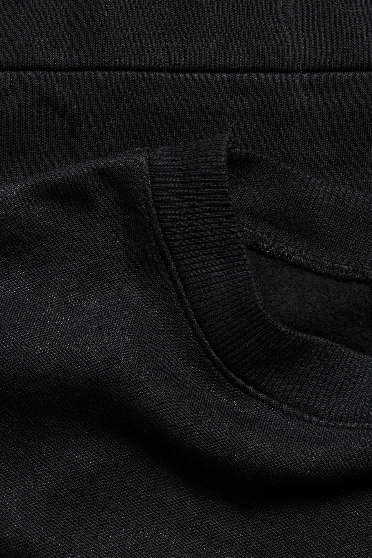 Zbliżenie na czarną bluzę dresową z dzianiny z prążkowanym okrągłym dekoltem.