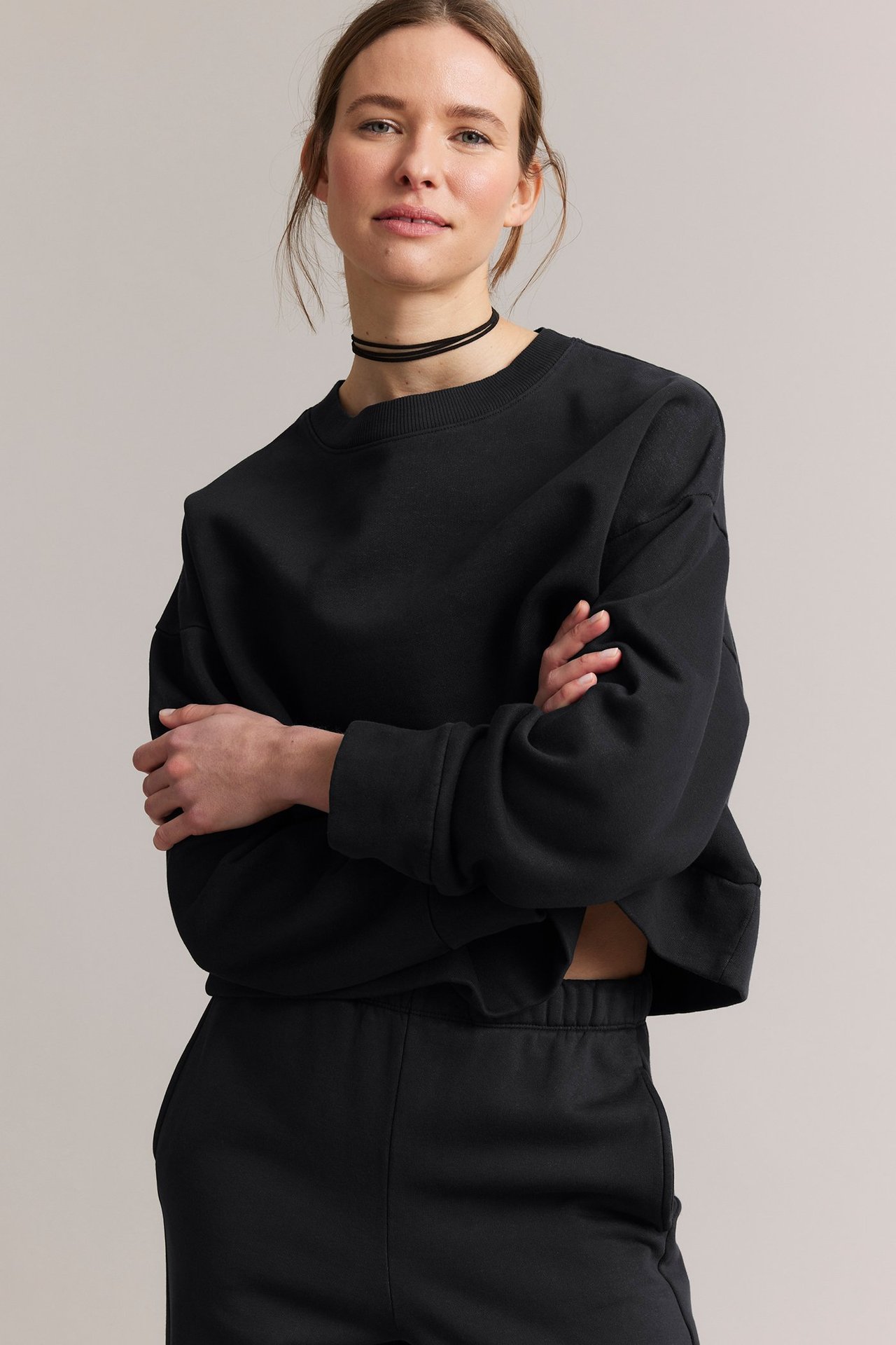 Forfra: kvinne i svart kort jerseystoffgenser, svarte joggebukser og svart chokerhalsbånd.