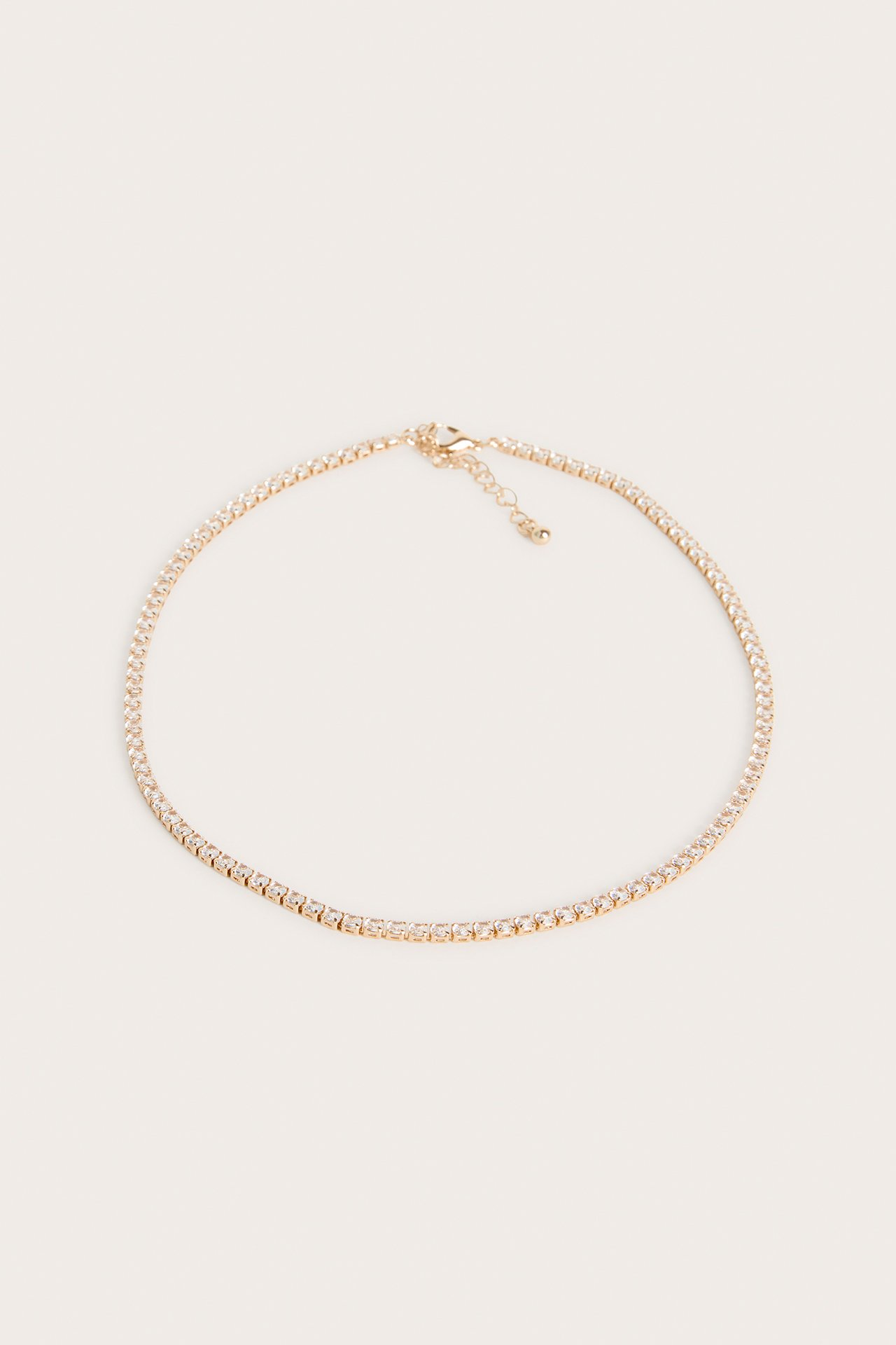 Närbild, uppifrån, av ett guldfärgat halsband med klara strasstenar och karbinhake.