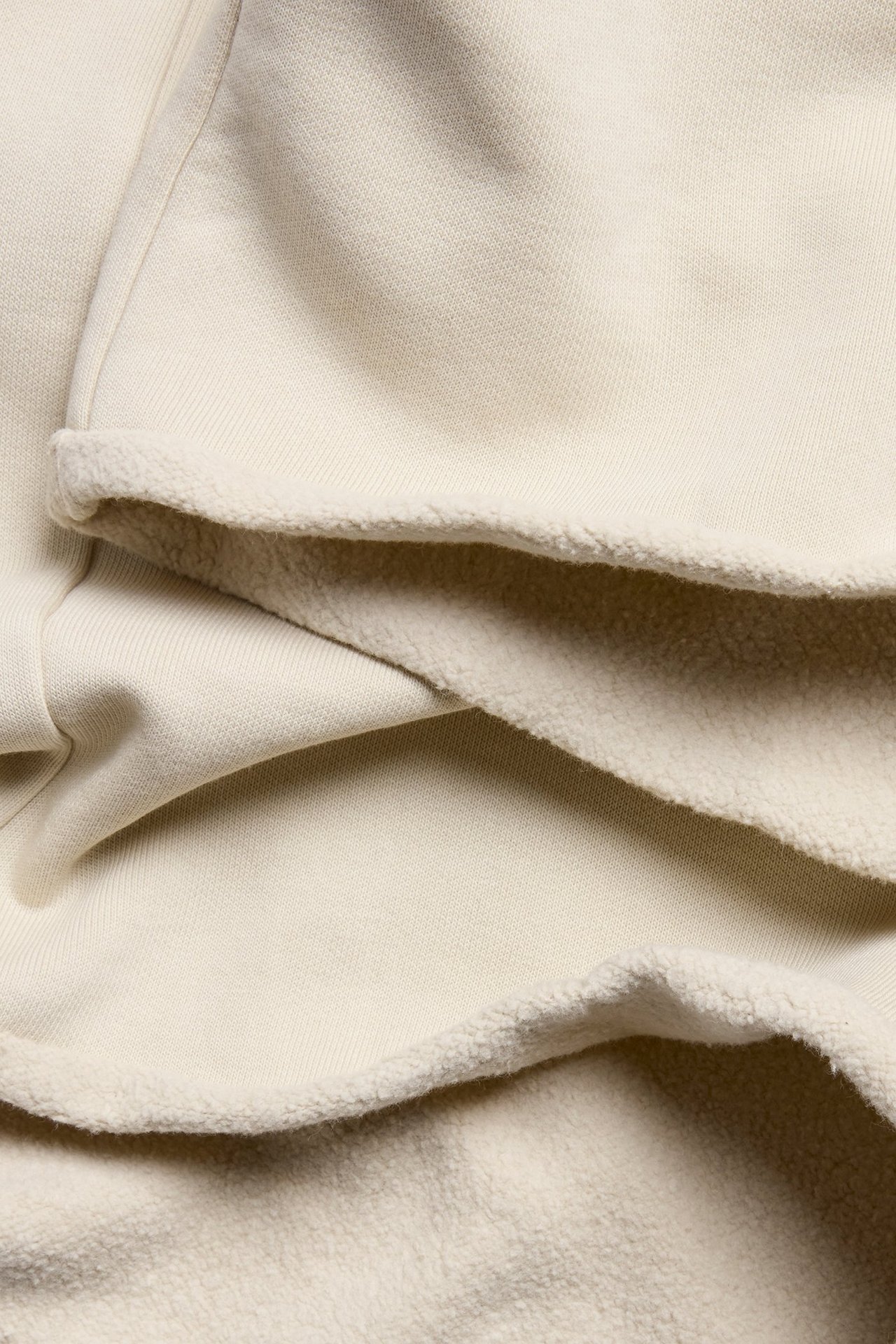 Zbliżenie na jasnobeżowy materiał dżersejowy, ukazujące gładką stronę zewnętrzną i miękką, szczotkowaną wewnętrzną.