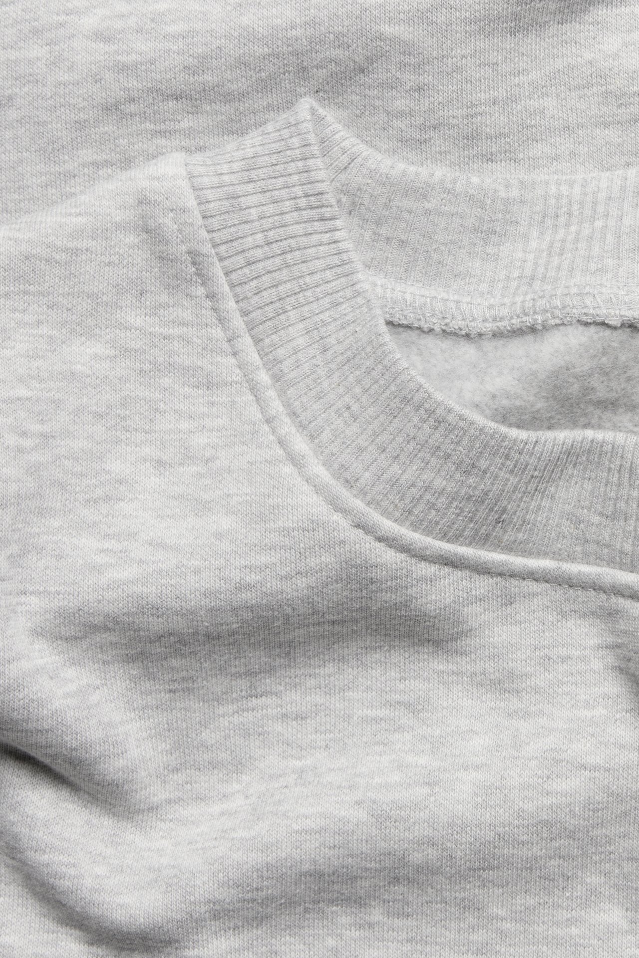 Nærbilde av en lys gråmelert lang sweatshirt med ribbet rund hals.