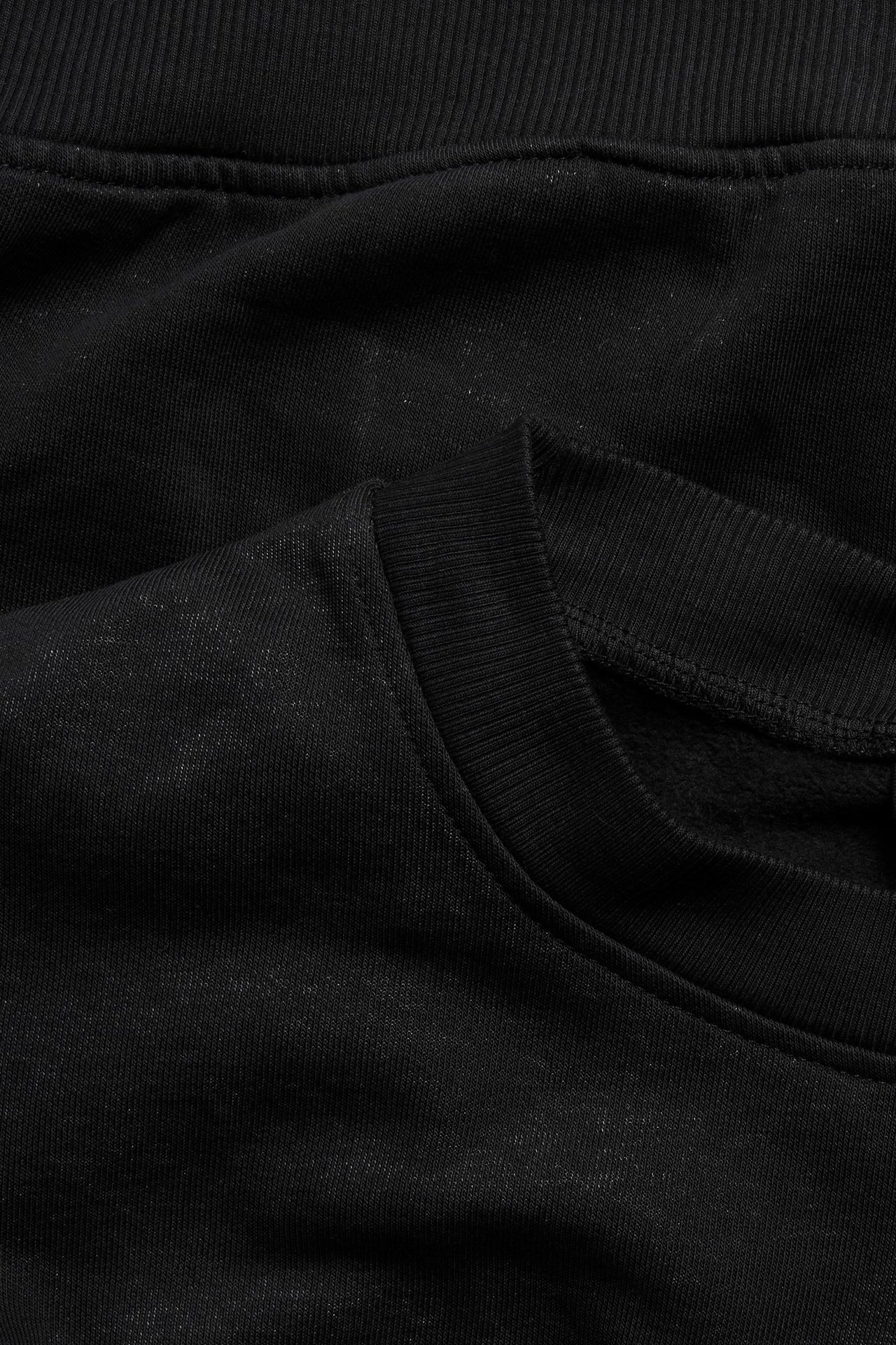Zbliżenie na czarną, długą bluzę dresową o spranej fakturze z prążkowanym kołnierzem.