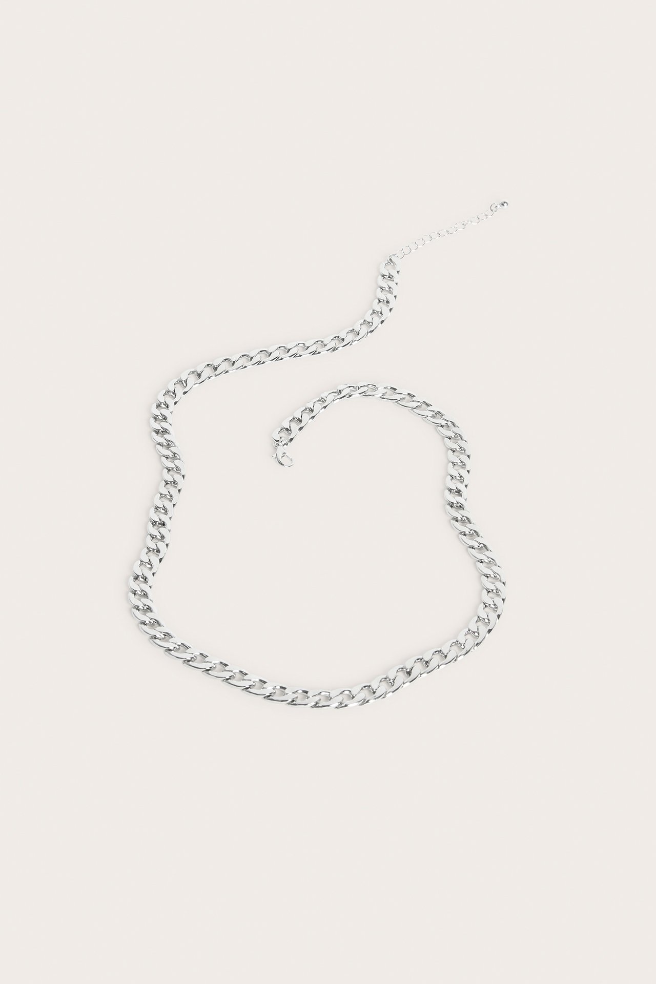 Ylhäältä kuvattu hopeanvärinen metallinen ketjukaulakoru, aseteltuna tasolle.
