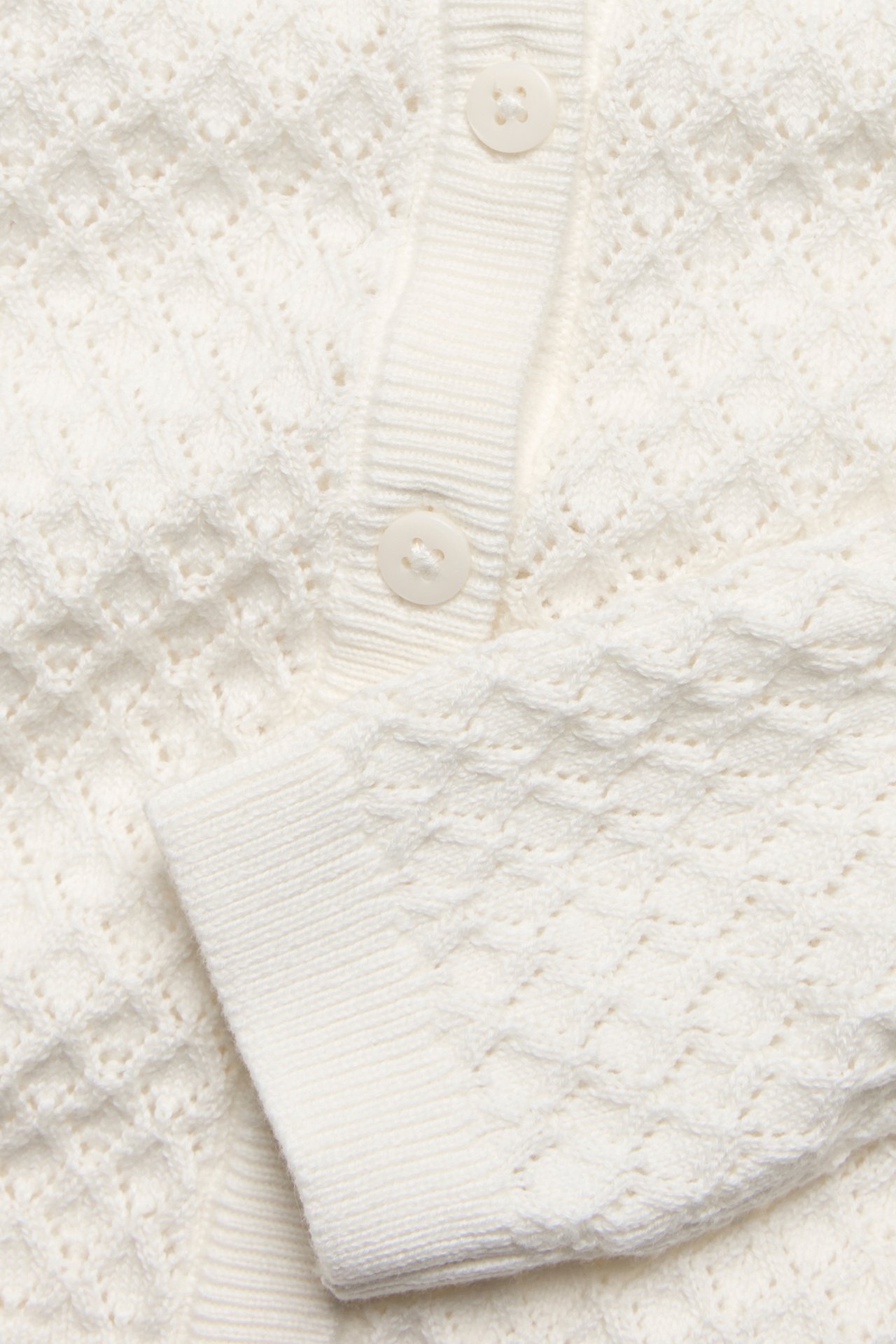Nærbilde av en offwhite mønsterstrikket cardigan med to knapper og ribbet mansjett.
