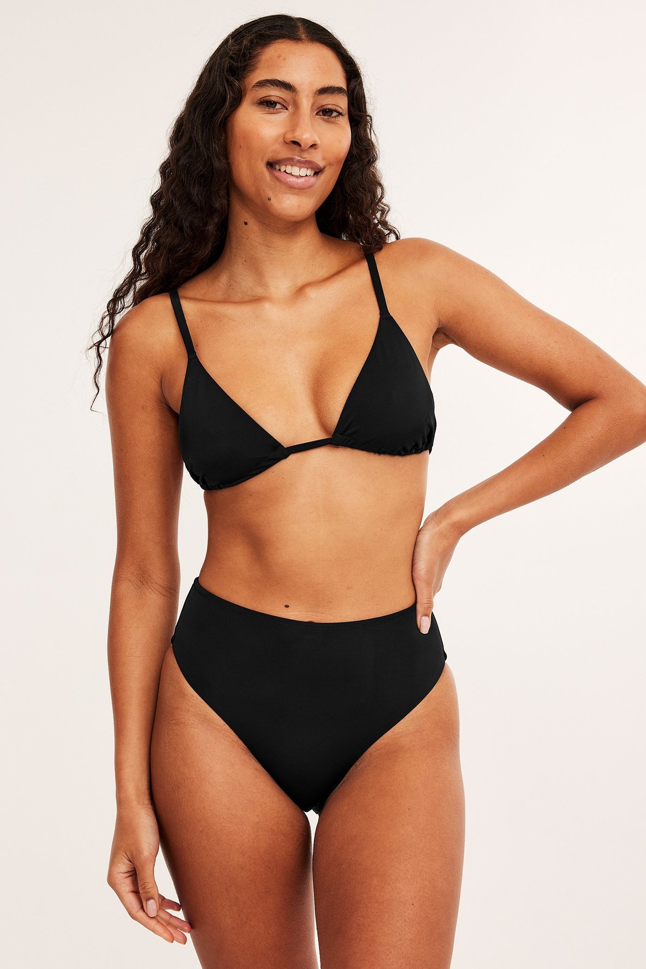 Widok z przodu: kobieta w czarnych, wysokich figach bikini brazilian i pasującym biustonoszu trójkątnym.