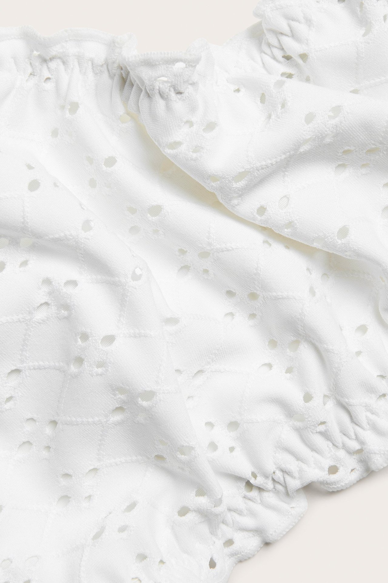 Zbliżenie na kremowy, żakardowy materiał od bikini z ażurowym wzorem i falbankami.