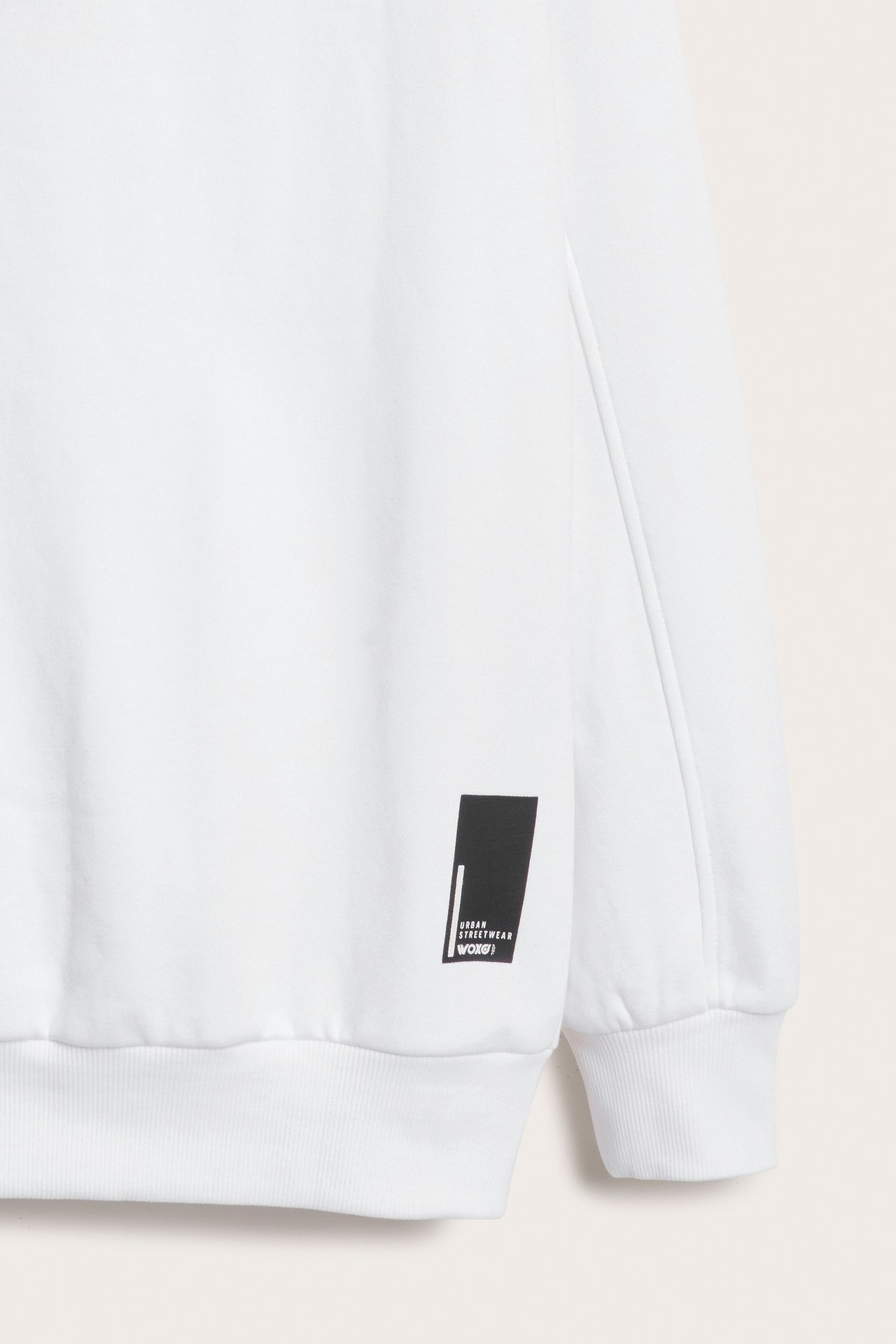 Närbild framifrån på en vit sweatshirt med svart rektangulärt "URBAN STREETWEAR WOXO" tryck.