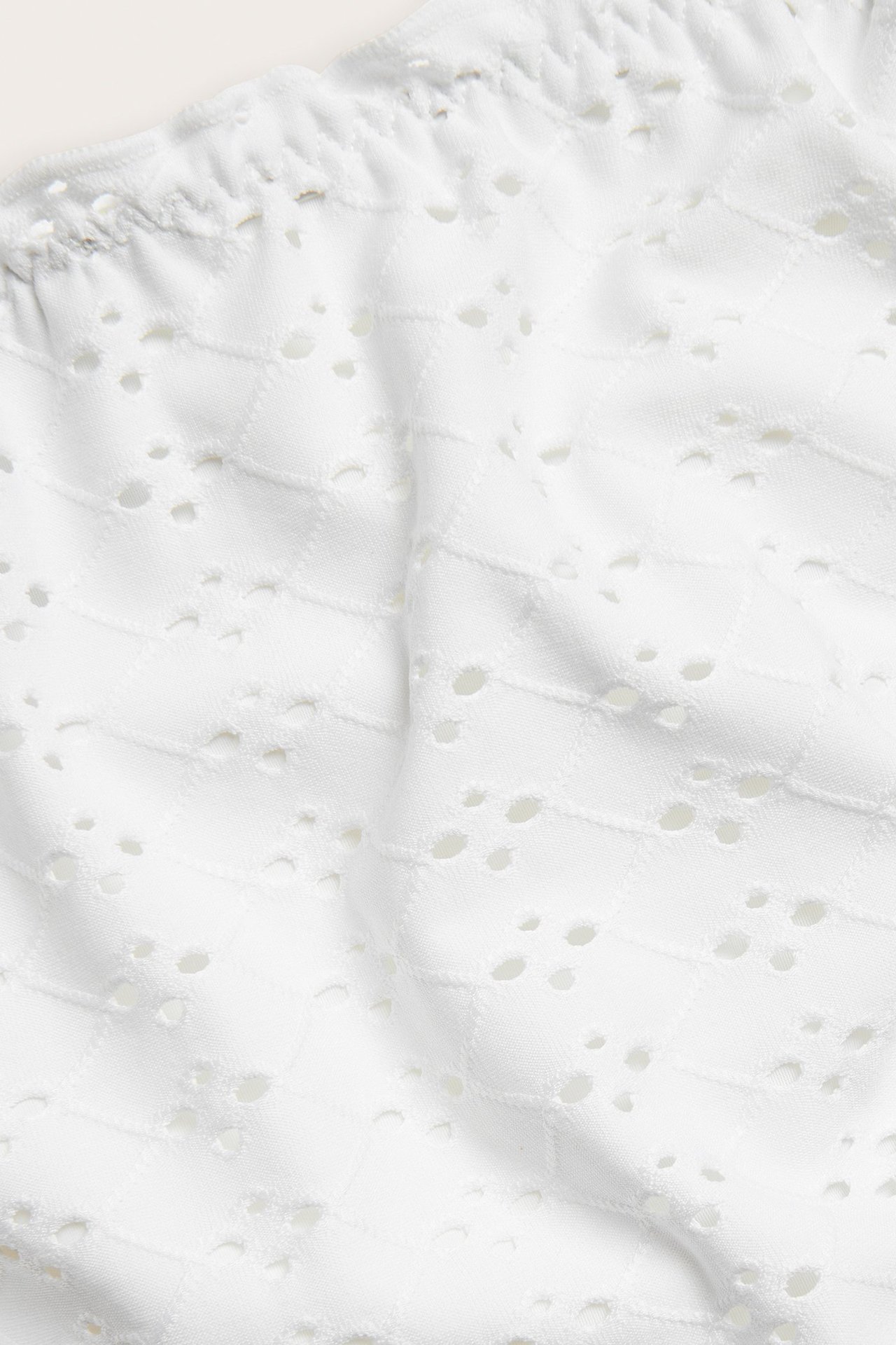 Zbliżenie na kremowe majtki bikini z teksturowanym wzorem żakardowym i małymi wycięciami.