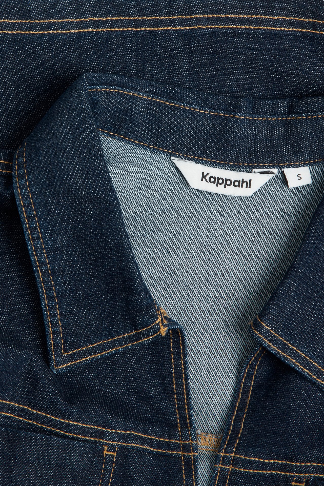 Lähikuva tummasta denim-puserosta, jossa on kaulus ja oranssinruskeat tikkaukset.